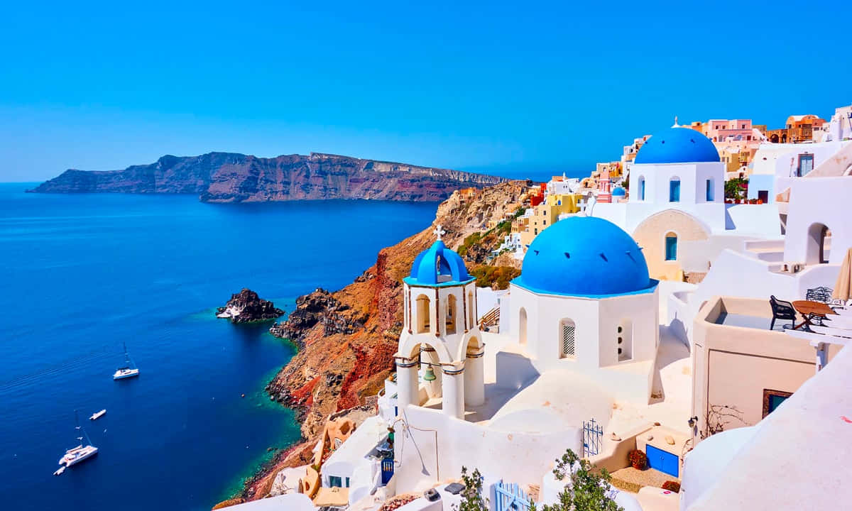 Greek Island 桌布 壁紙 — 白色建築物配以鮮豔的藍色圓頂，戲劇性地棲息在俯瞰深藍色愛琴海的懸崖上。