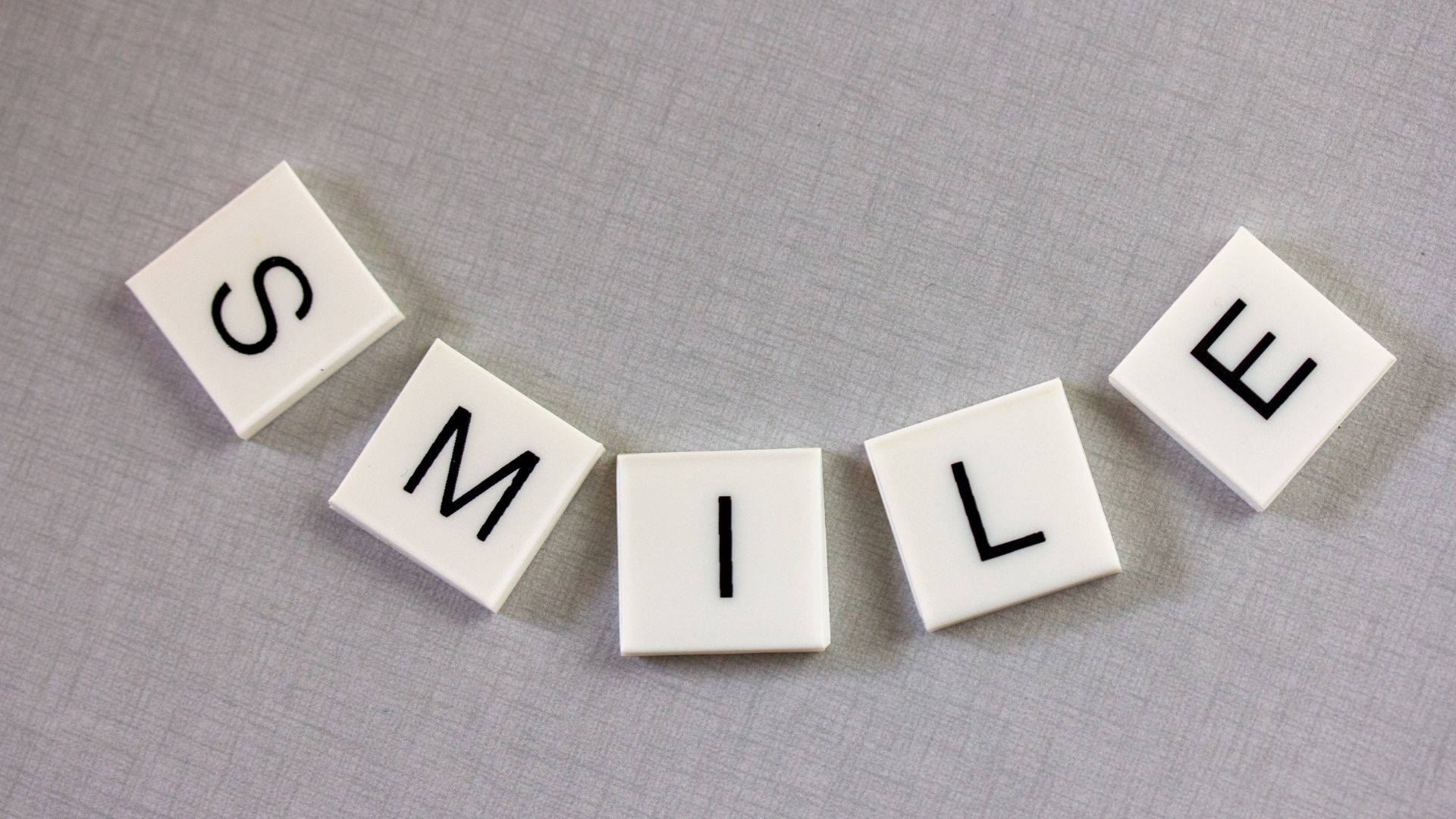 Smile 桌布 壁紙 — 白色方形瓷磚在帶紋理的灰色布料表面上用粗體黑色字母拼出 smile。