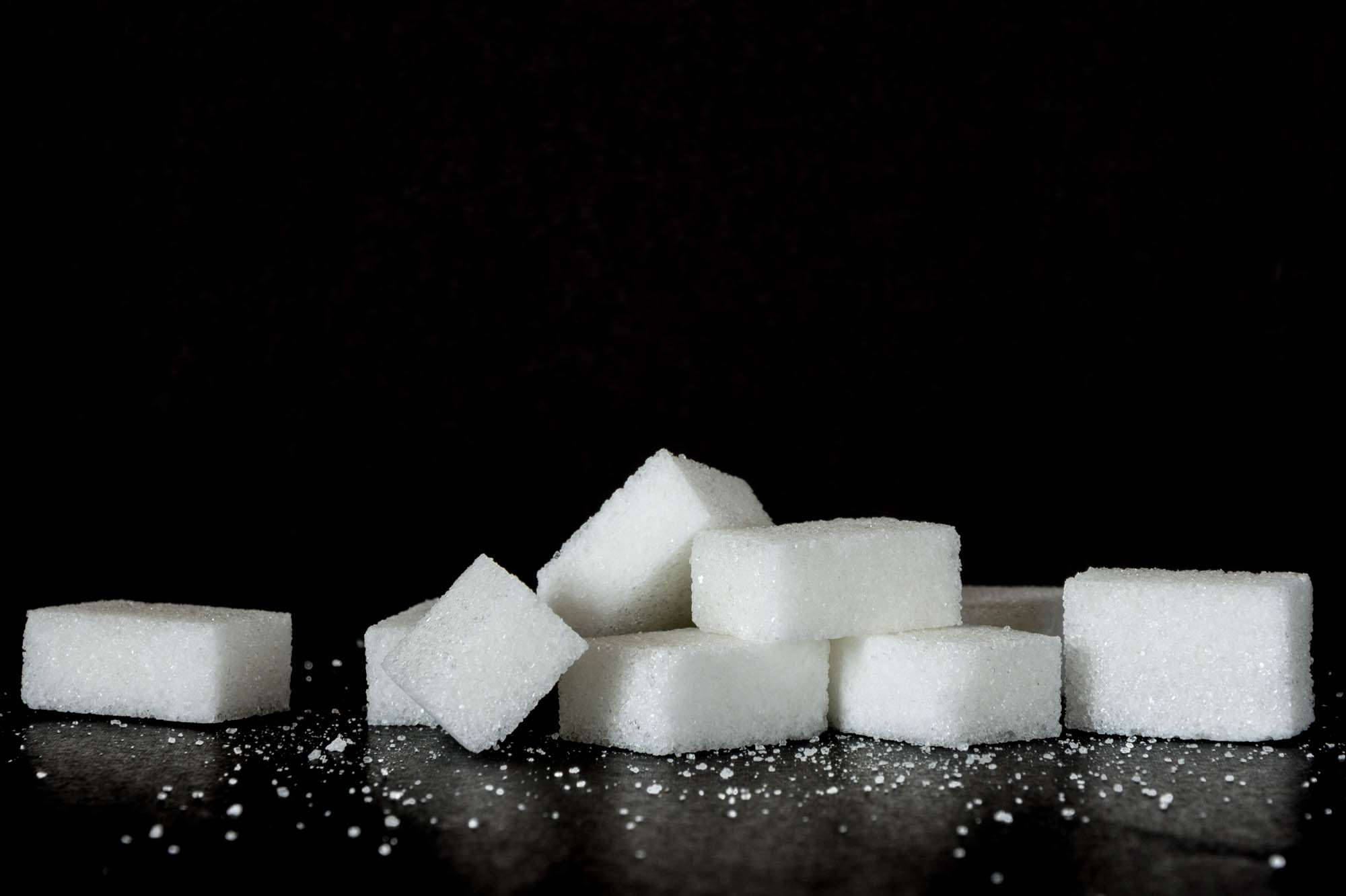Sugar 桌布 壁紙 — 白色方糖堆疊在深色表面上，散落著顆粒，背景為黑色。