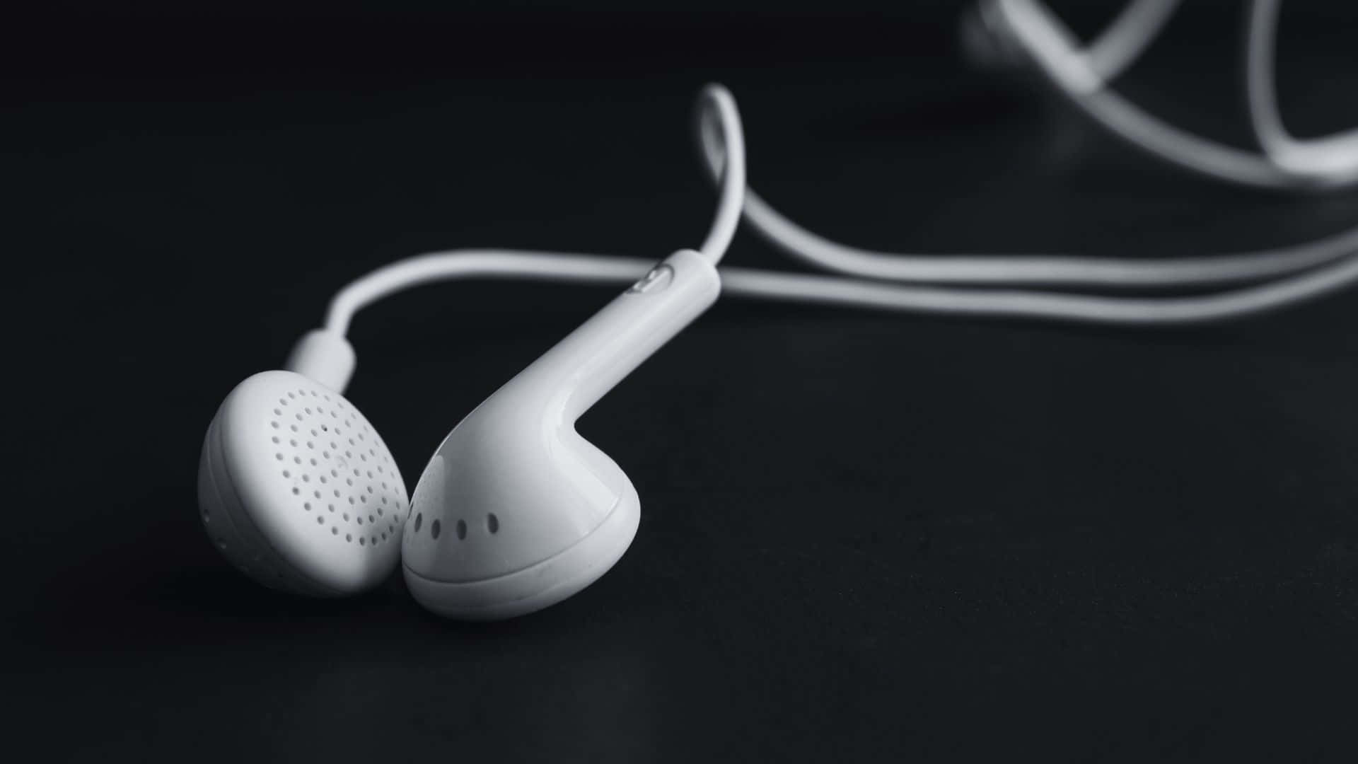 Black And White Music 桌布 壁紙 — 白色有線耳機放置在深色表面上，帶有柔和陰影和淺景深。