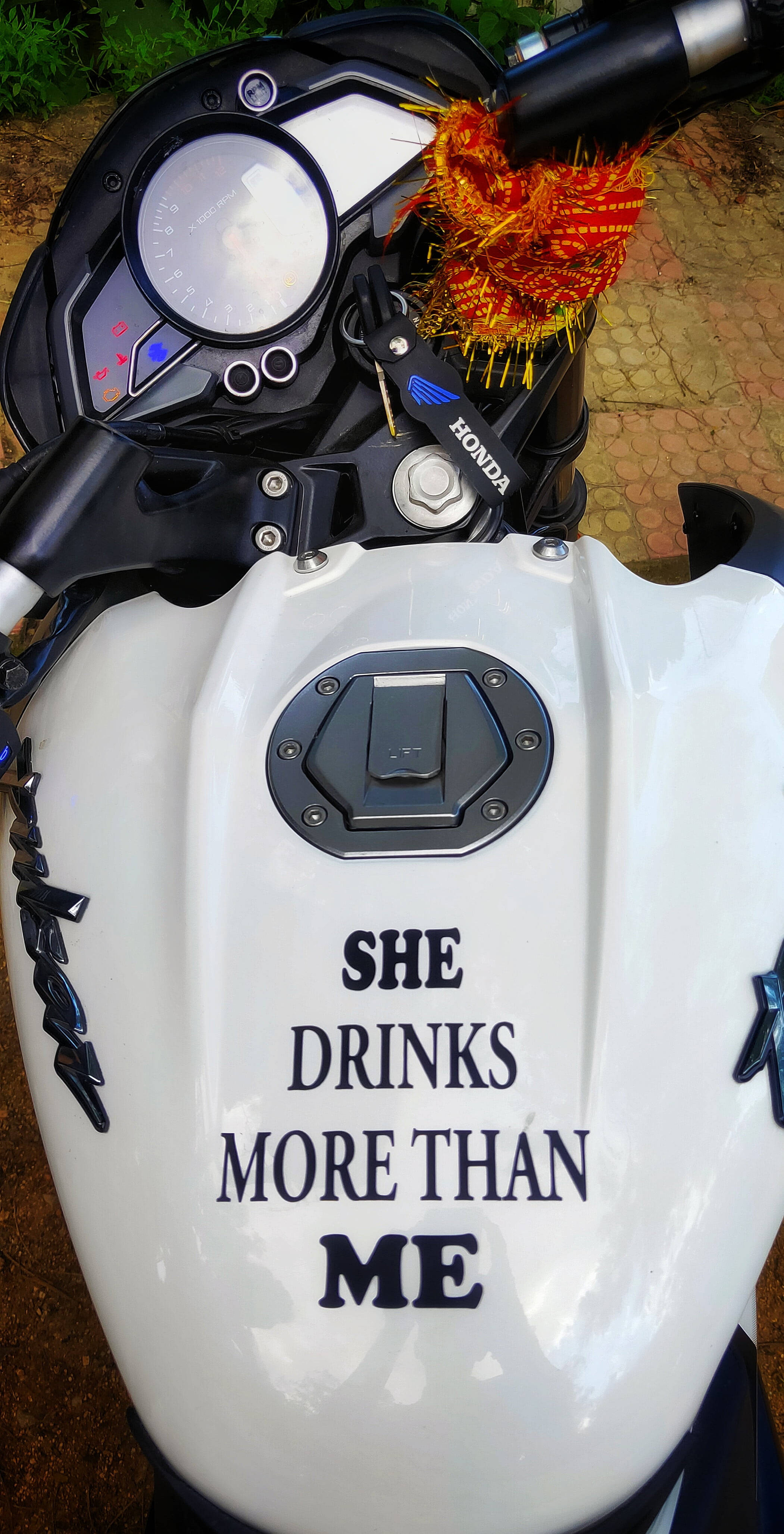 機車 桌布 壁紙 — 白色本田機車油箱特寫，粗體字寫著「SHE DRINKS MORE THAN ME」，手把上有紅橙色裝飾流蘇。