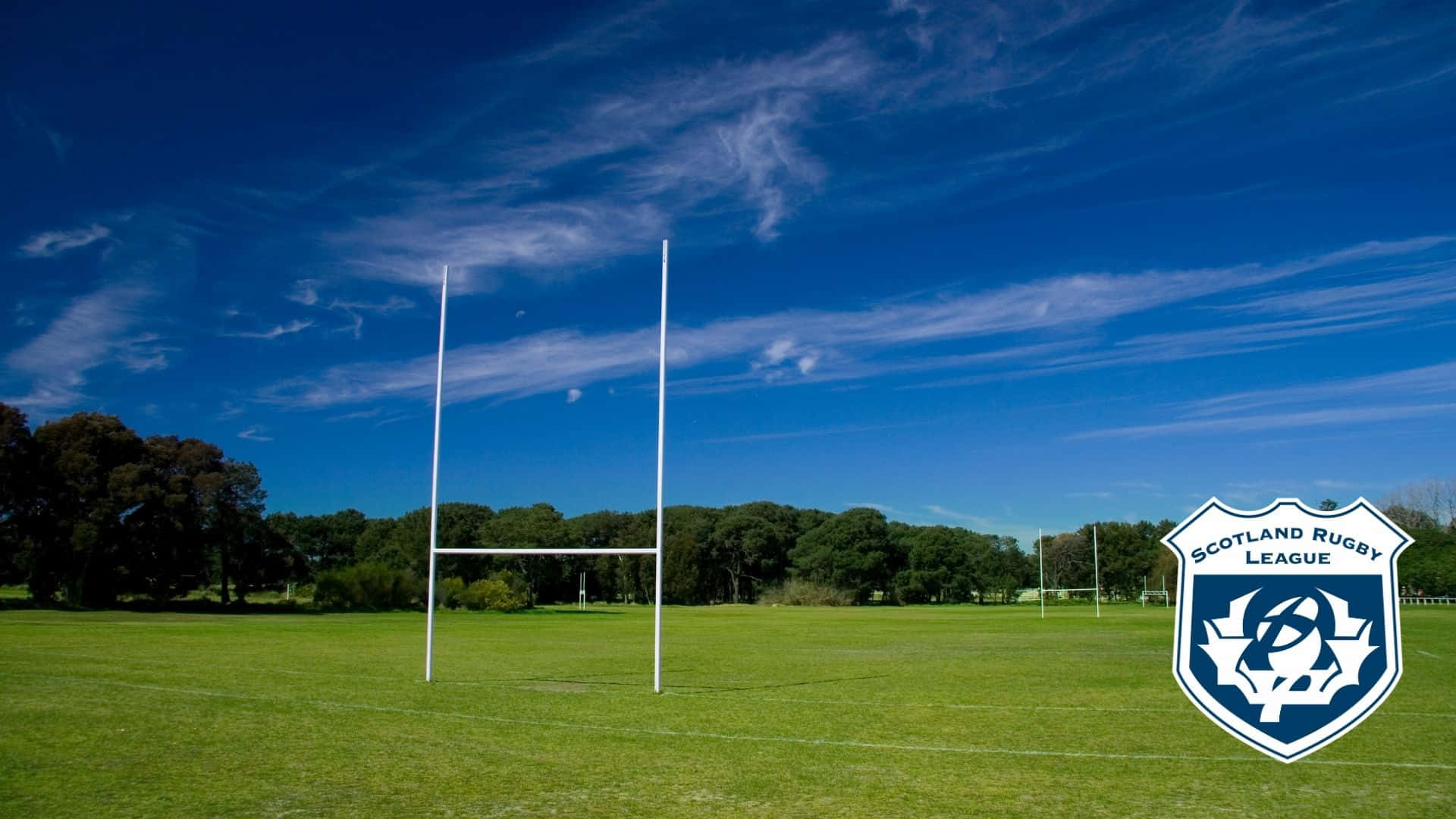 Scotland Rugby 桌布 壁紙 — 白色橄欖球柱在晴朗藍天和薄雲下，聳立在充滿活力的綠色球場上。