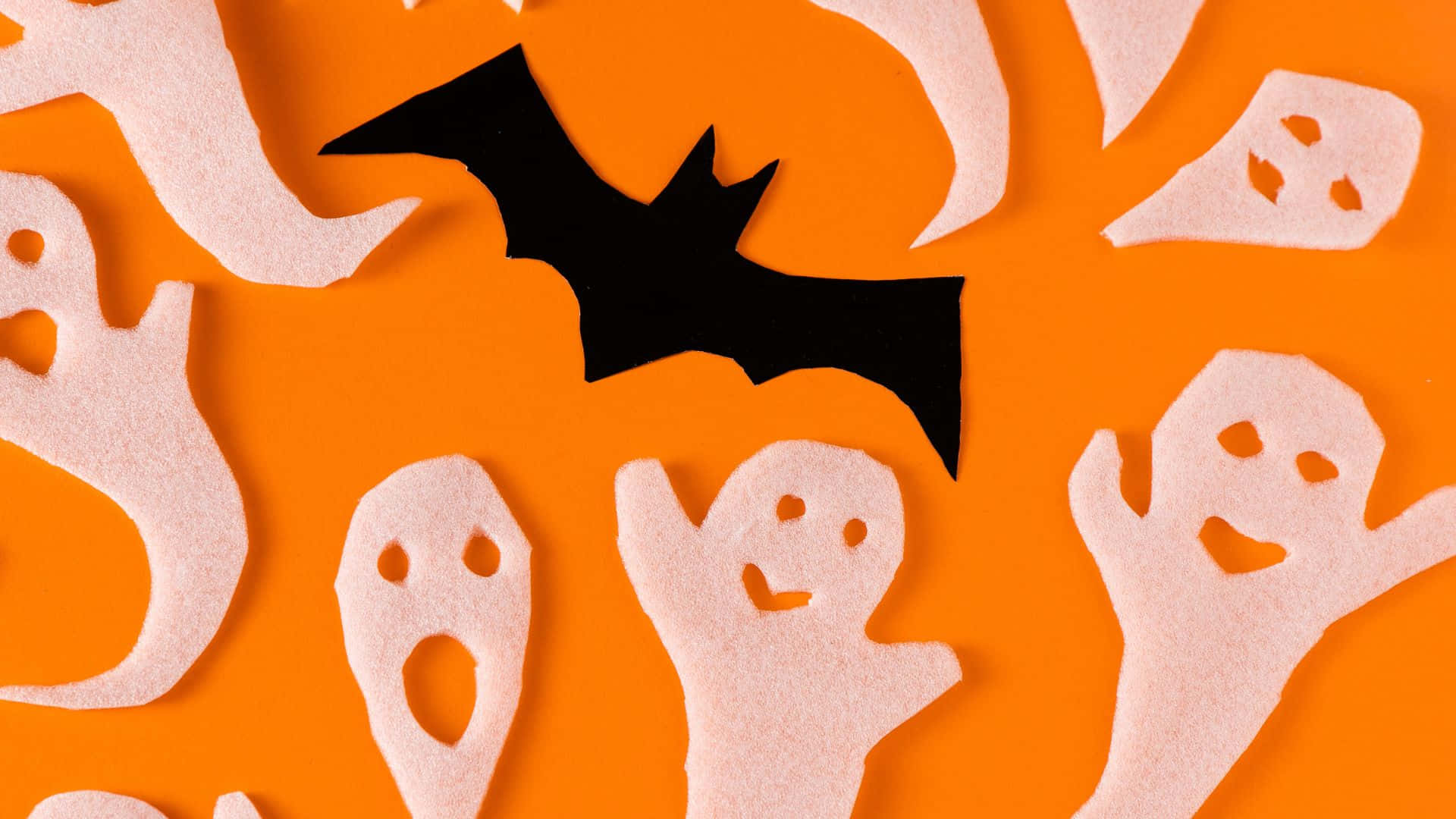Halloween Crafts 桌布 壁紙 — 白色氈布鬼魂和一隻黑色蝙蝠在鮮豔的橙色背景上頑皮地漂浮。