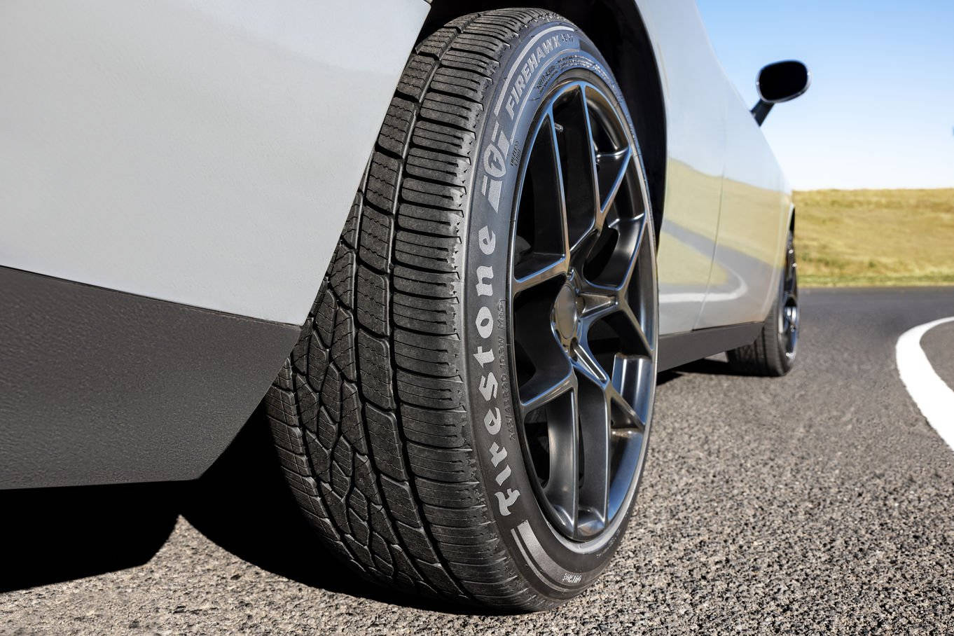 Firestone 桌布 壁紙 — 白色汽車輪胎和合金輪圈在蜿蜒的瀝青路上、明亮日光下的特寫。