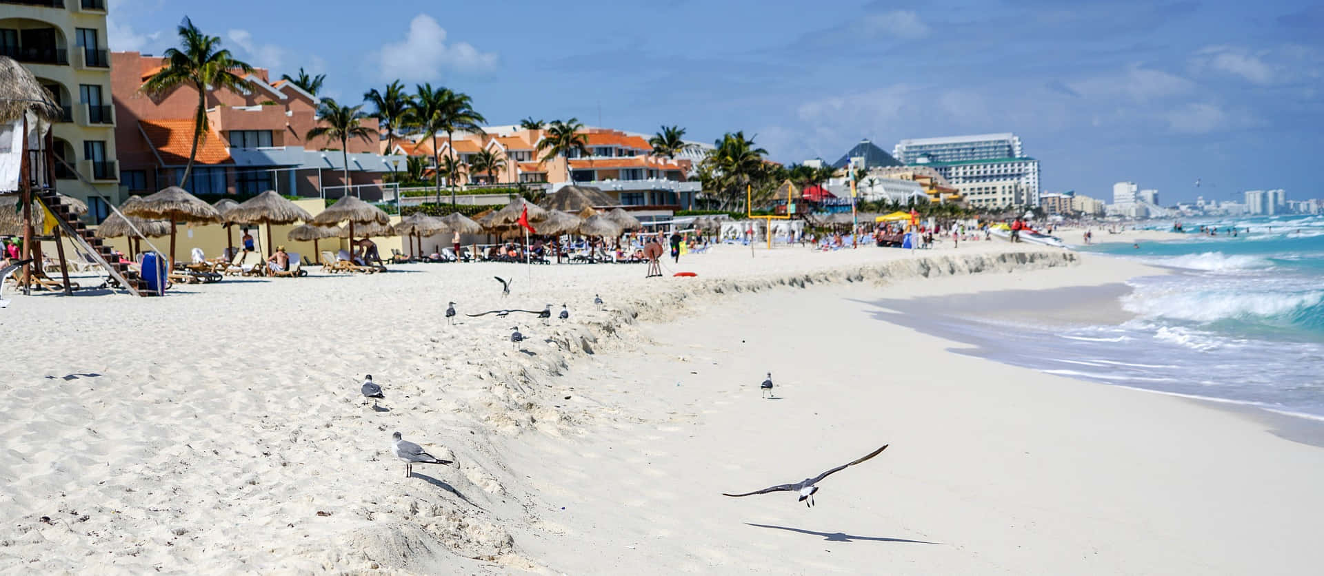 Cancun 桌布 壁紙 — 白色沙灘，碧綠海浪拍打岸邊度假村和棕櫚樹，天空湛藍明亮。