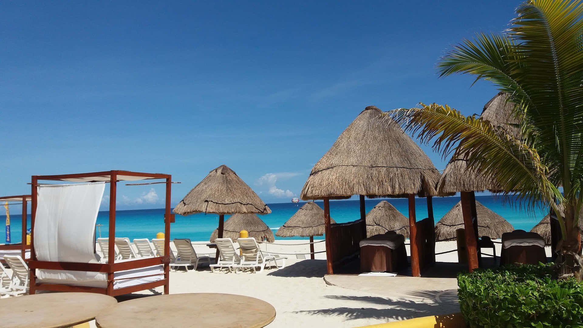 Cancun 桌布 壁紙 — 白色沙灘上排列著茅草遮陽傘和躺椅，上方是清澈的藍天和碧綠的海洋。