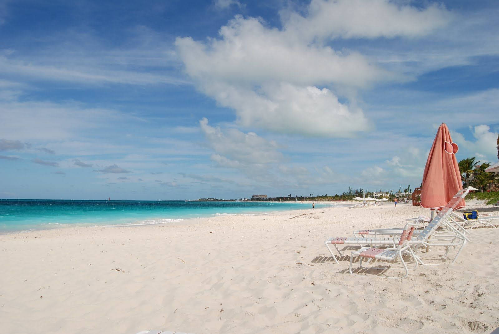Turks And Caicos 桌布 壁紙 — 白色沙灘與碧綠海洋，在明亮藍天下有蓬鬆雲朵和粉紅色遮陽傘。