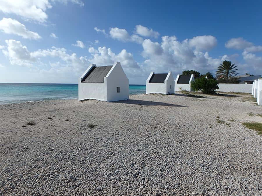 Hut 桌布 壁紙 — 白色海灘小屋配深色屋頂，矗立在卵石灘上，藍天白雲。