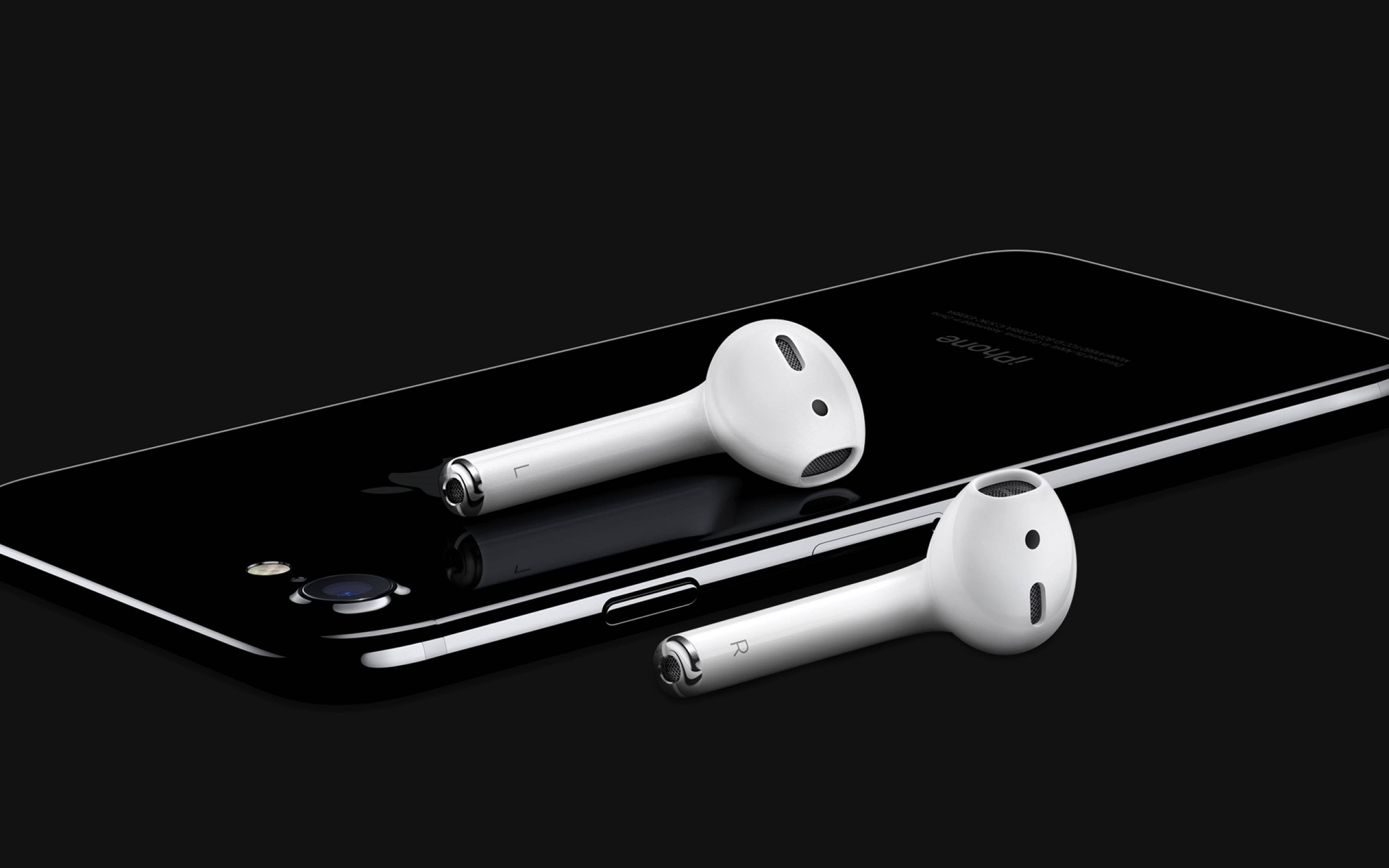AirPods 桌布 壁紙 — 白色無線耳塞優雅地放置在時尚的黑色智慧型手機上，背景為深色。