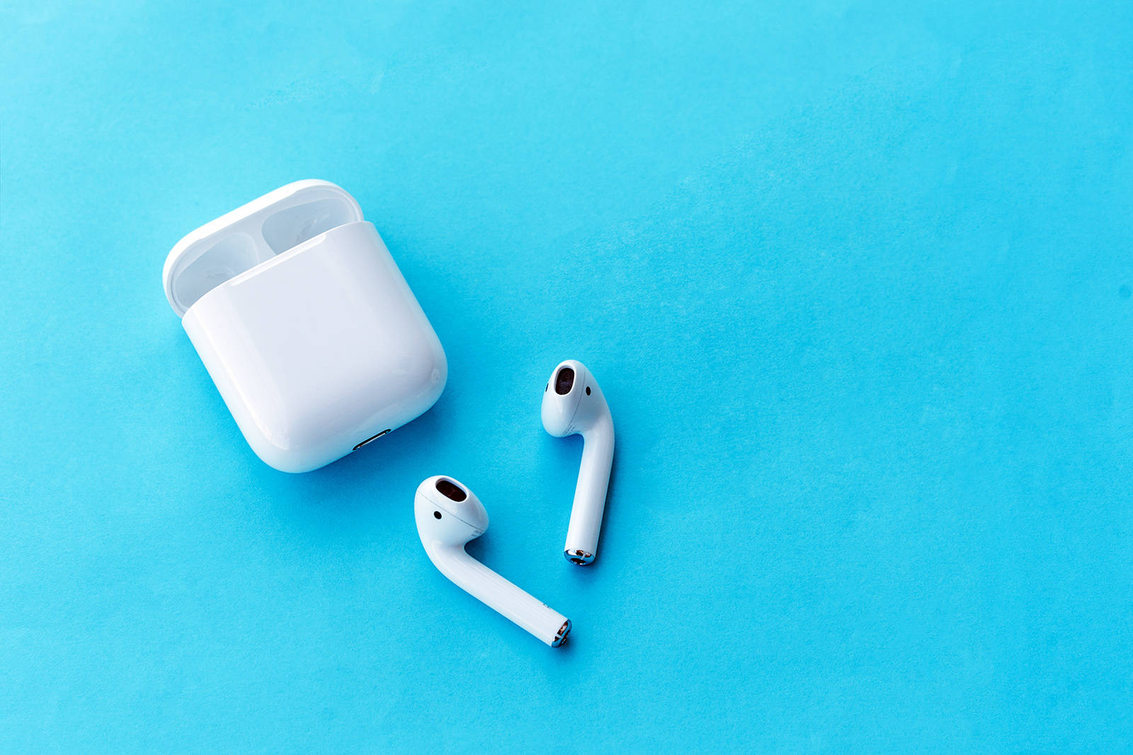 Airpods 桌布 壁紙 — 白色無線耳機及其充電盒放置在純藍色紋理表面上。