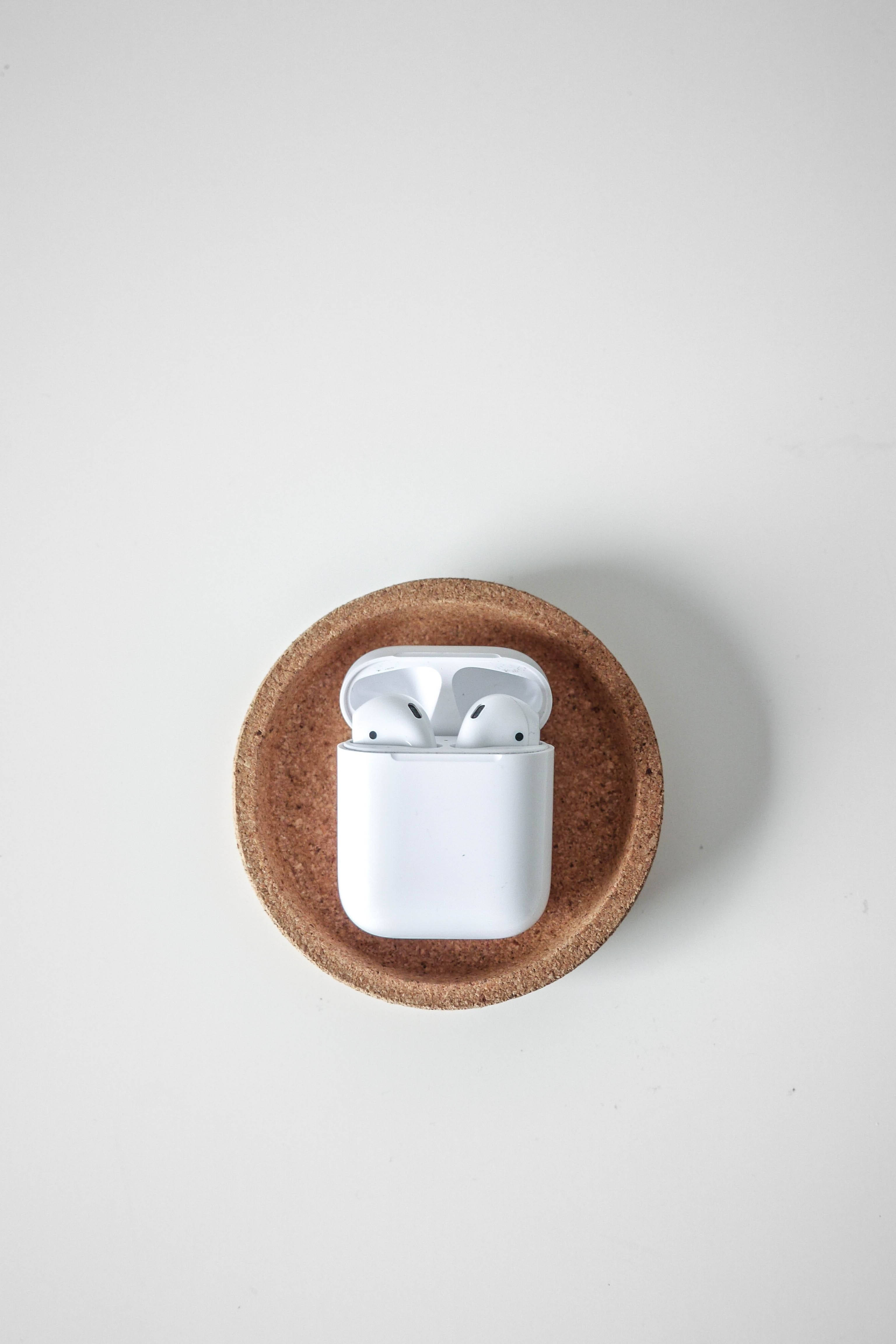 Airpods 桌布 壁紙 — 白色無線耳機放在打開的充電盒中，擱在圓形軟木杯墊上，背景為純白色。