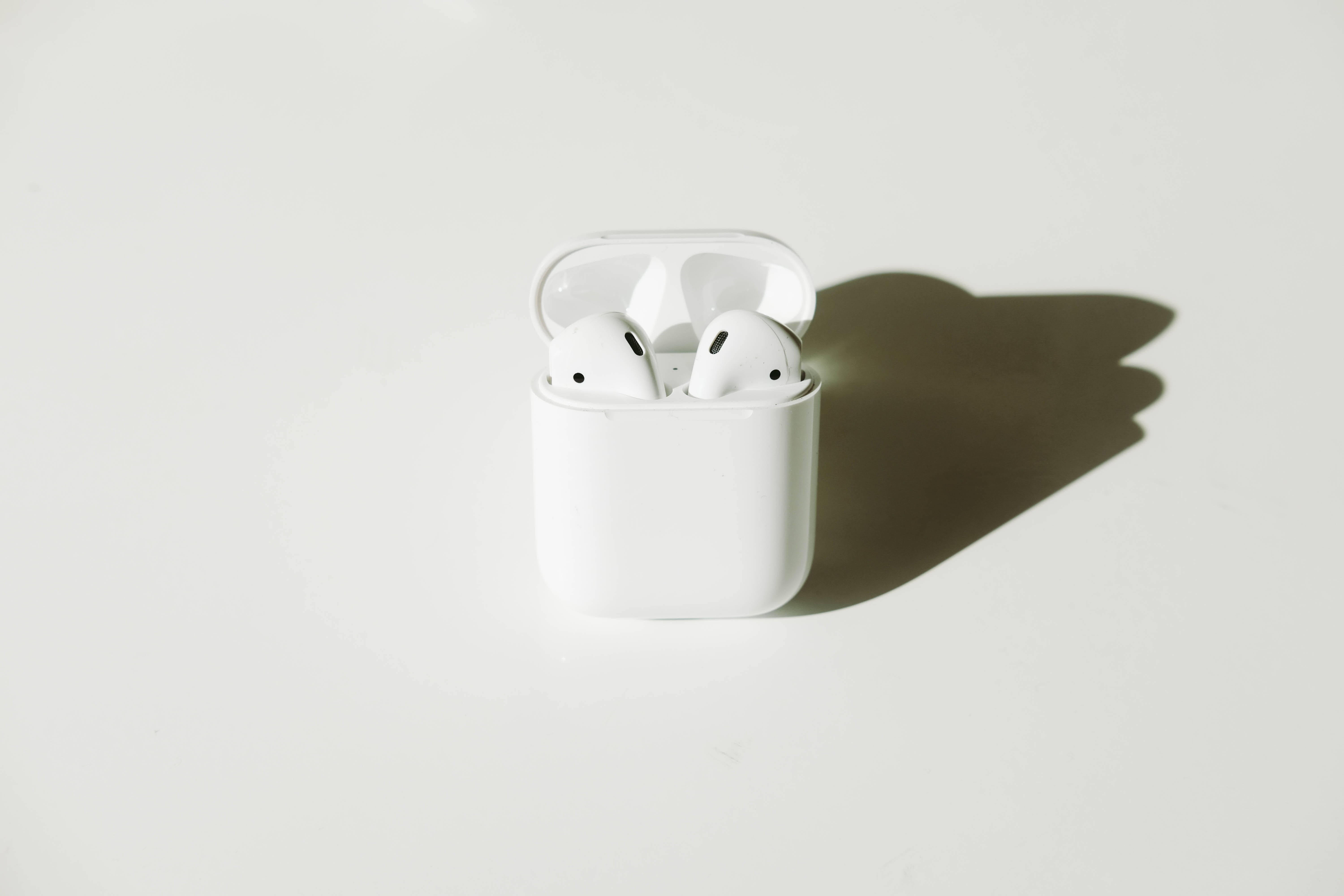 AirPods 桌布 壁紙 — 白色無線耳機整齊地放在打開的充電盒中，在極簡白色表面上投下清晰的陰影。
