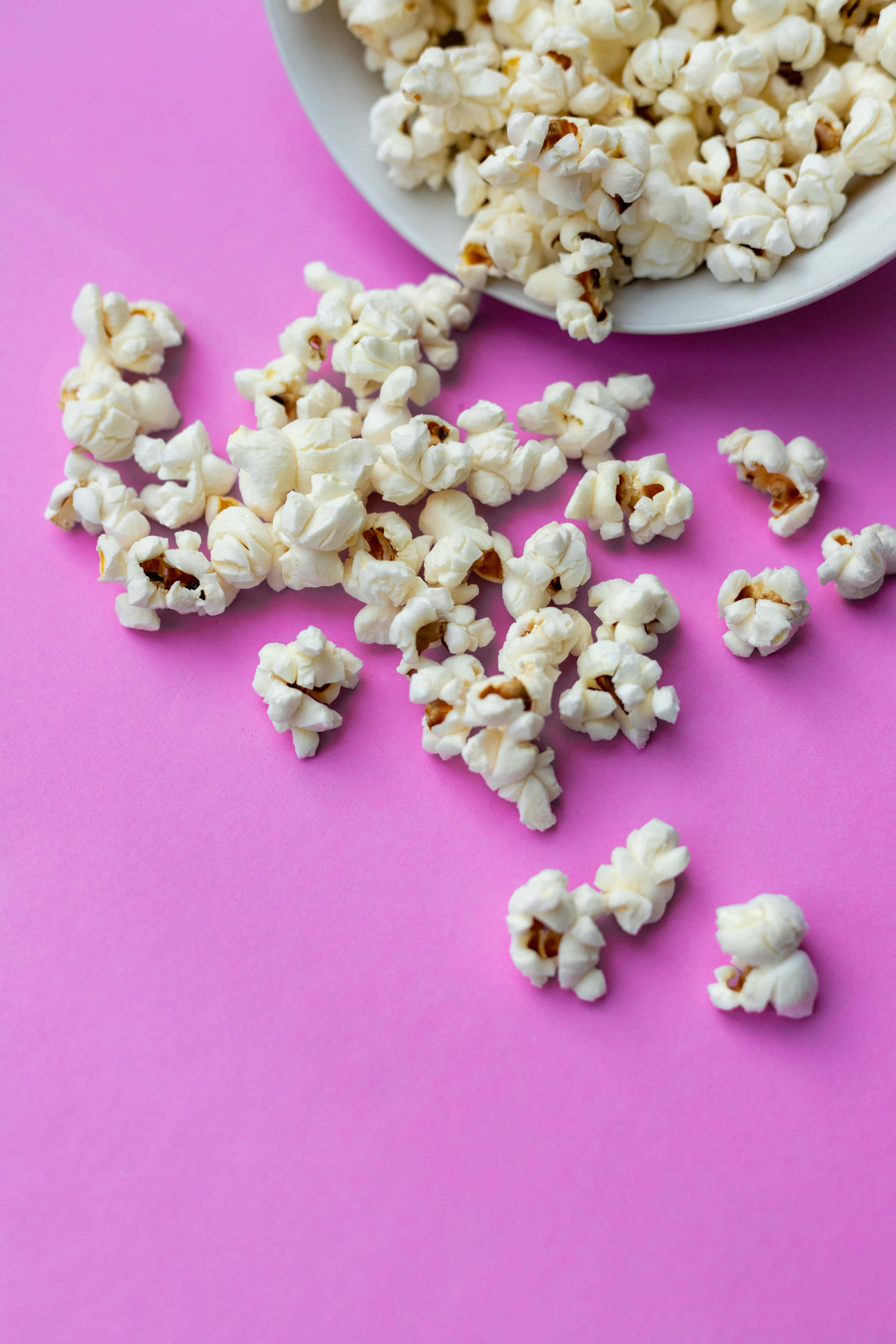 Popcorn 桌布 壁紙 — 白色爆米花粒從碗中灑落在鮮粉紅色表面上，形成平鋪構圖。