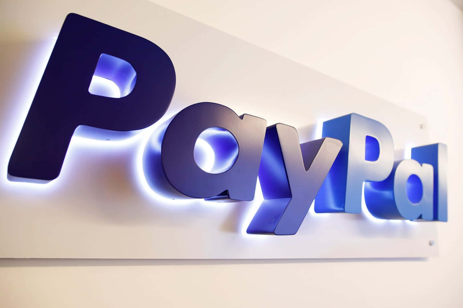 PayPal 桌布 壁紙 — 白色牆上安裝的發光藍色PayPal標誌特寫，字母亮起。