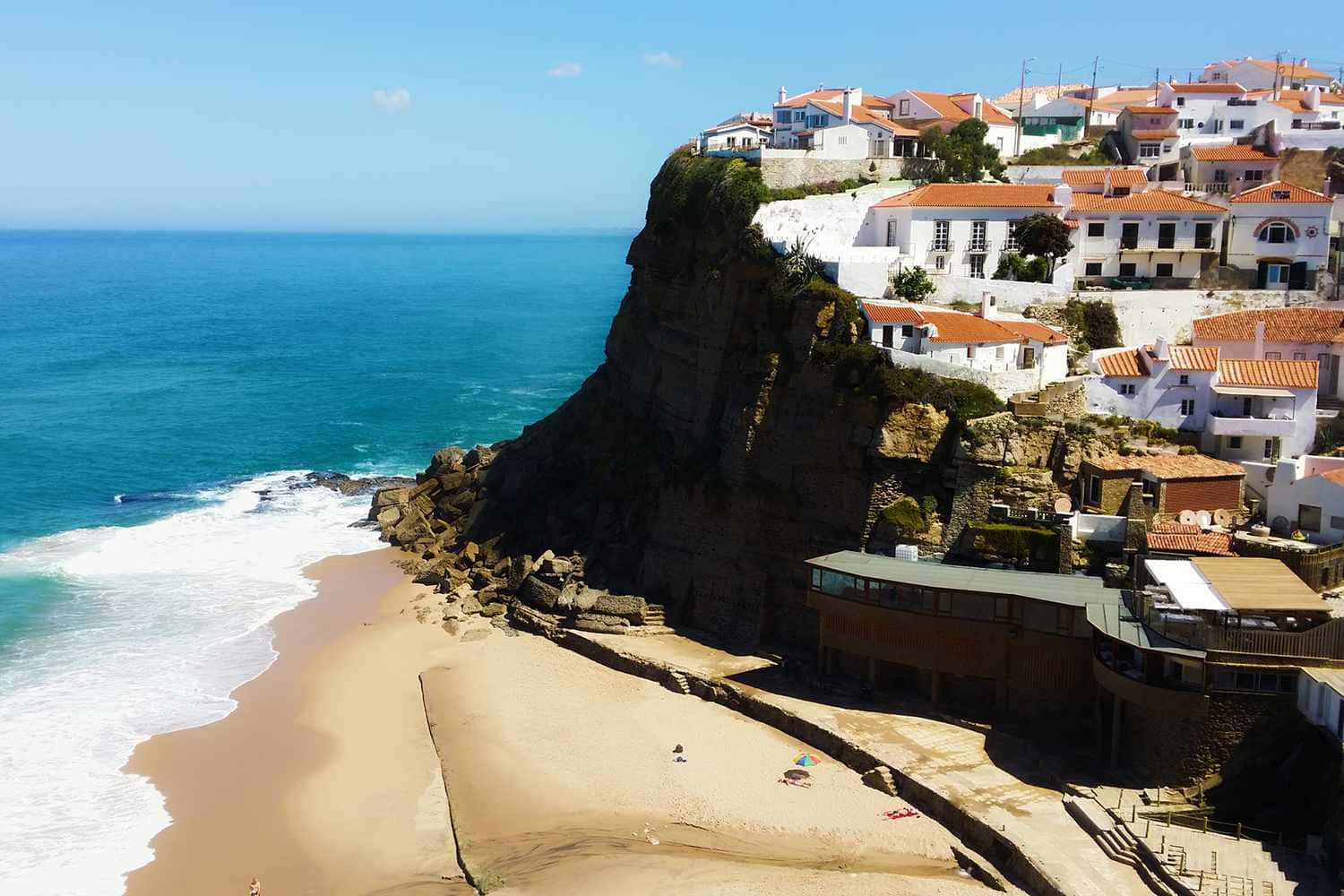 Portuguese Beach 桌布 壁紙 — 白色牆壁、陶土屋頂的房屋依附在崎嶇的懸崖上，俯瞰著碧綠的海洋和沙灘。