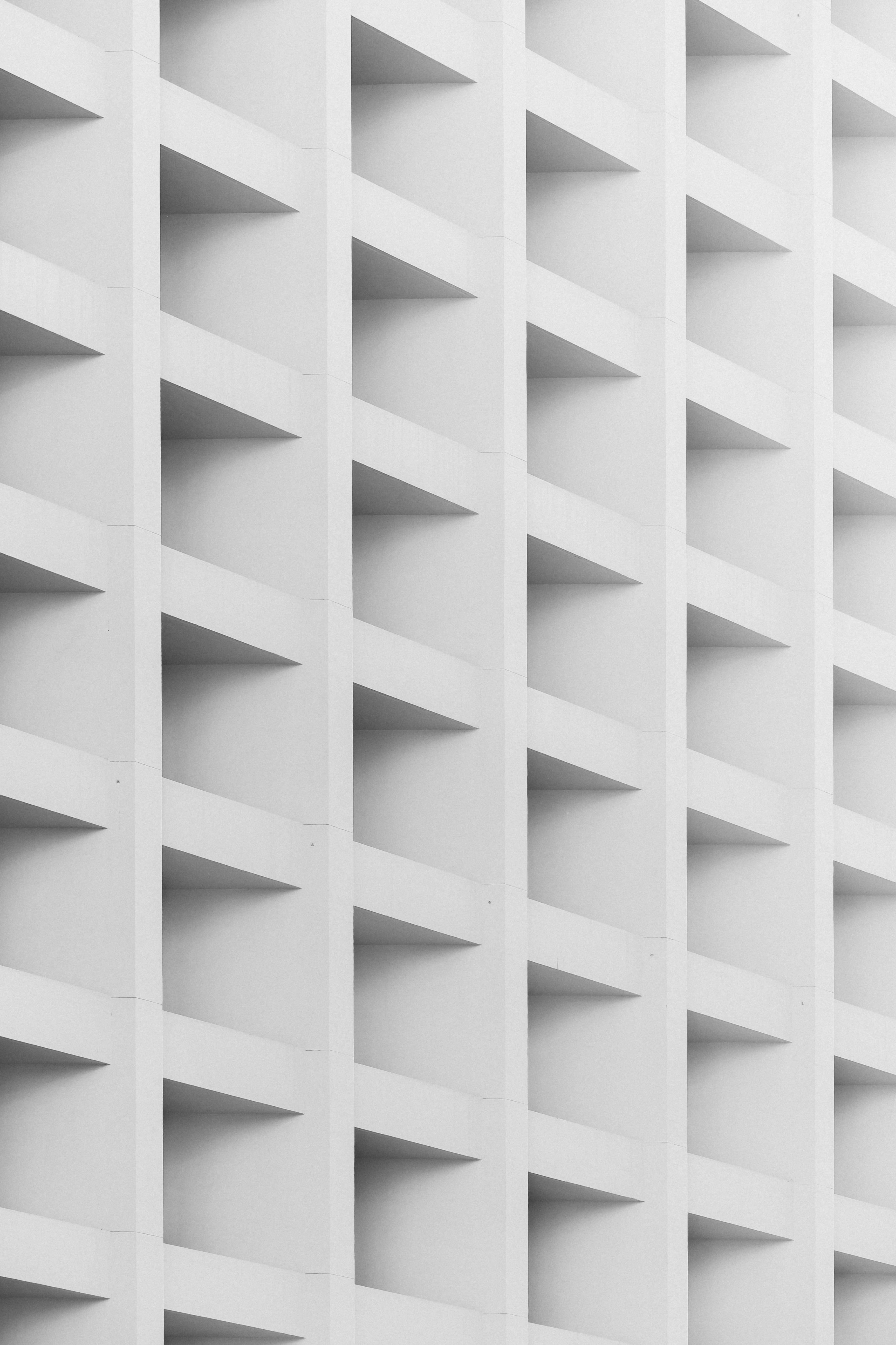 Geometric 桌布 壁紙 — 白色現代建築物外牆的特寫，重複的幾何凹陷面板形成強烈的線性陰影。