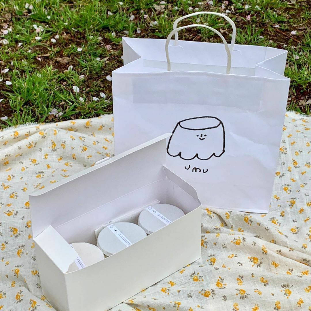 Pastries 桌布 壁紙 — 白色盒子和袋子，上面有可愛的果凍吉祥物，坐在草地和落花瓣中的花卉毯子上。
