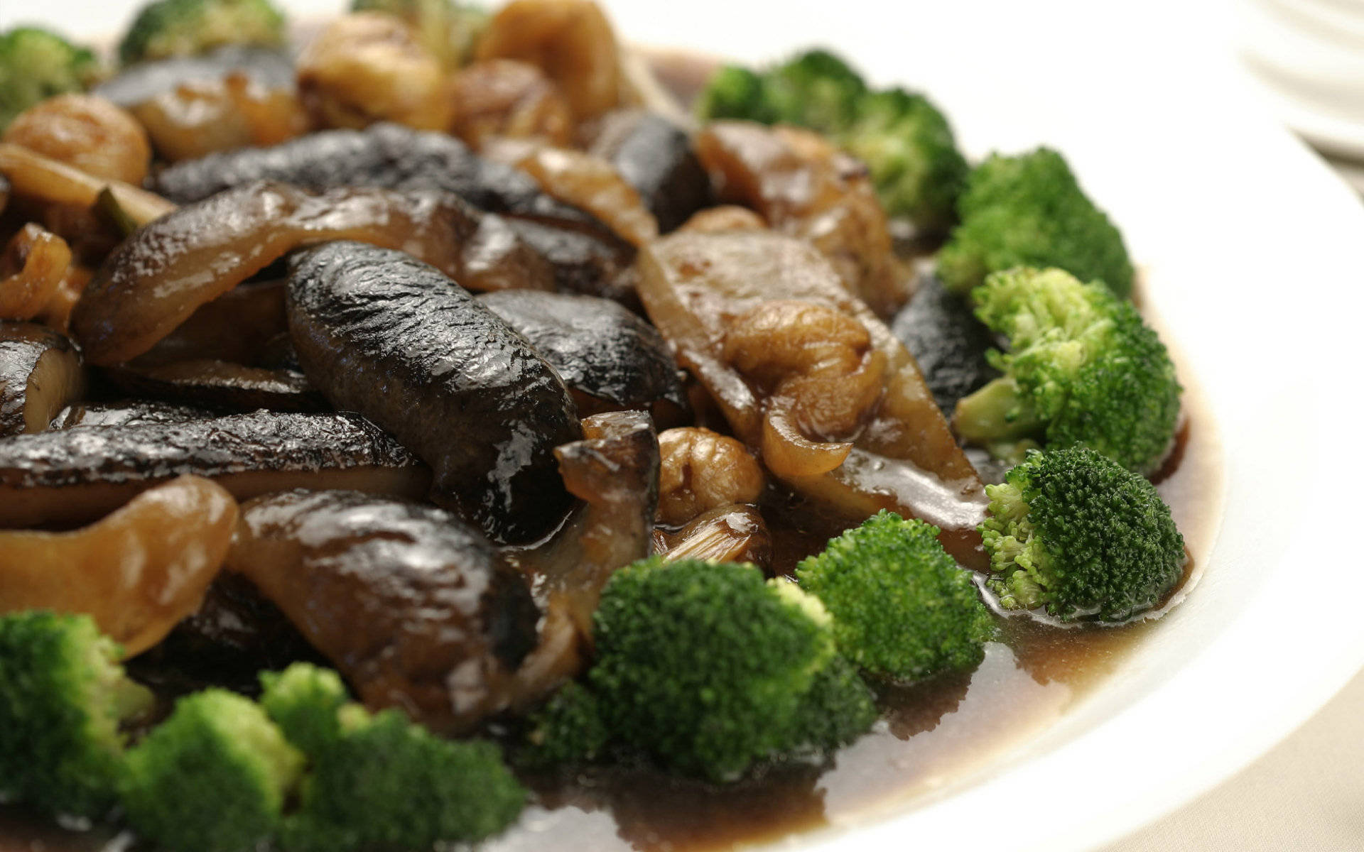 4K Food 桌布 壁紙 — 白色盤子上光澤的炒蘑菇和鮮綠色西蘭花小朵，搭配濃郁棕色醬汁的特寫。