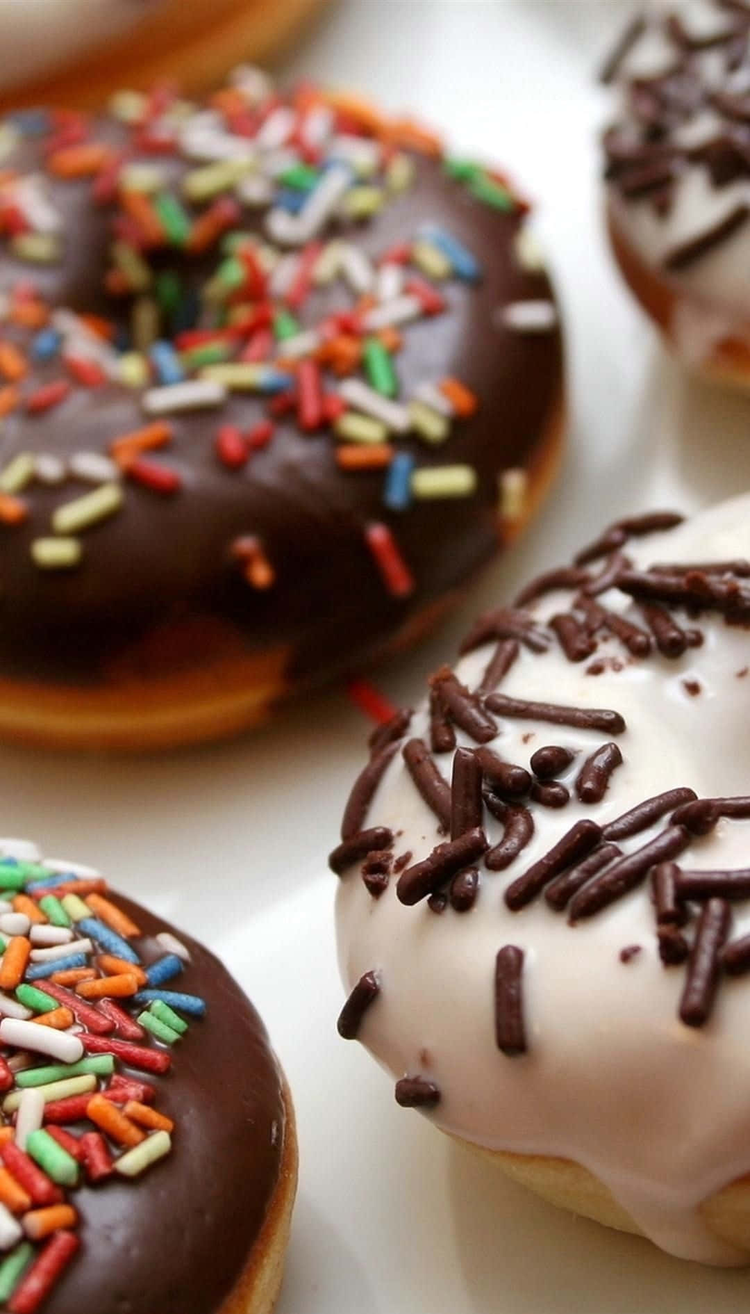 Donut 桌布 壁紙 — 白色盤子上巧克力與香草甜甜圈的近照，上面撒有彩色糖粒和巧克力醬。