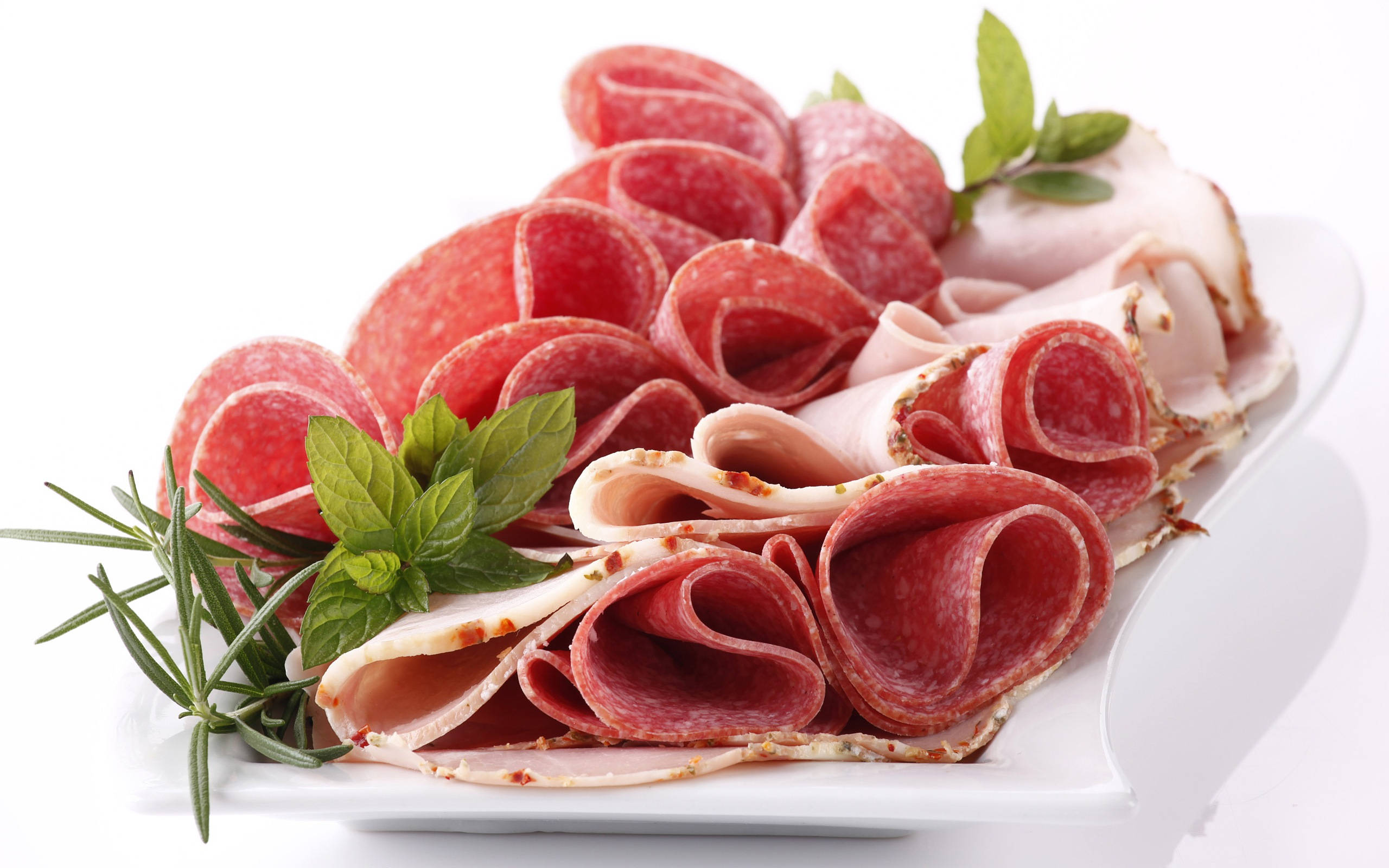 Ham 桌布 壁紙 — 白色盤子上擺放著精心排列的莎樂美腸和火腿卷片，並以新鮮迷迭香和薄荷點綴。