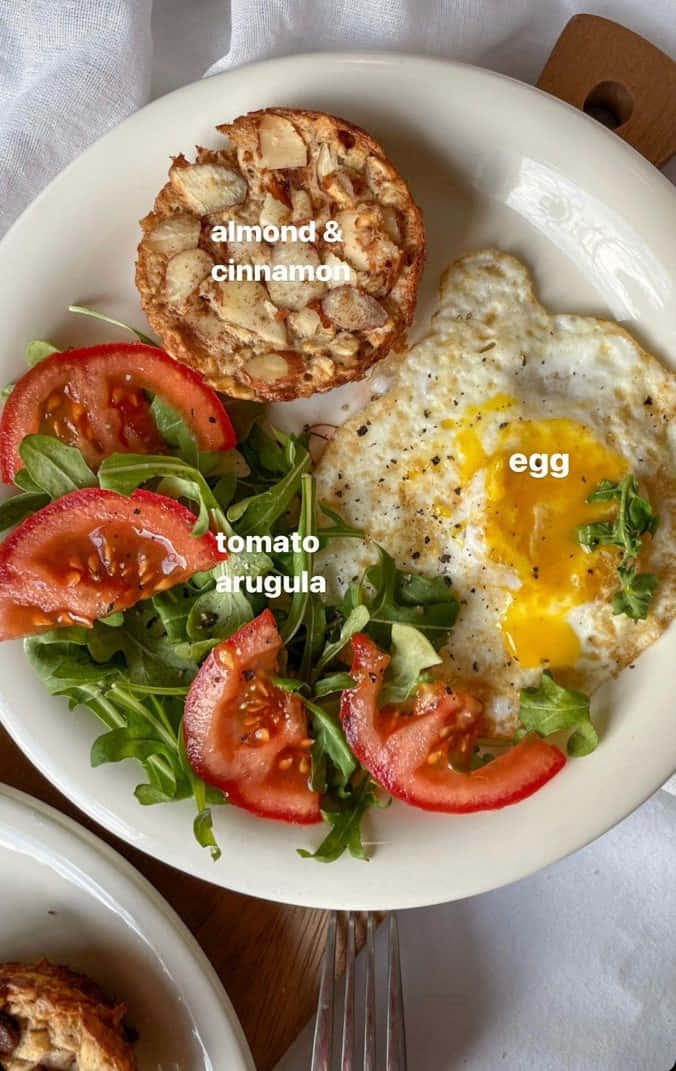 Minimalist Food 桌布 壁紙 — 白色盤子上放有太陽蛋、切片番茄、芝麻葉和杏仁肉桂馬芬，置於亞麻桌布上。