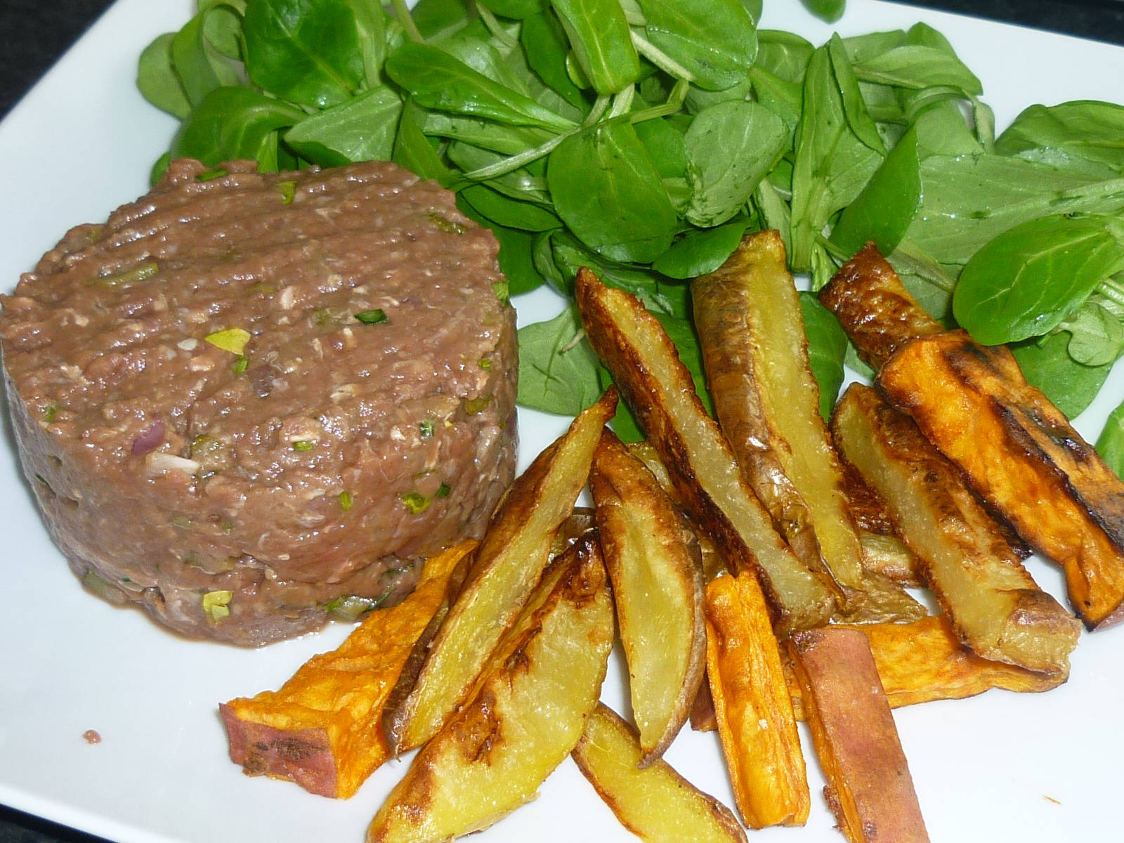 meat 桌布 壁紙 — 白色盤子上放有生牛肉他他肉餅、新鮮菠菜和烤地瓜條。