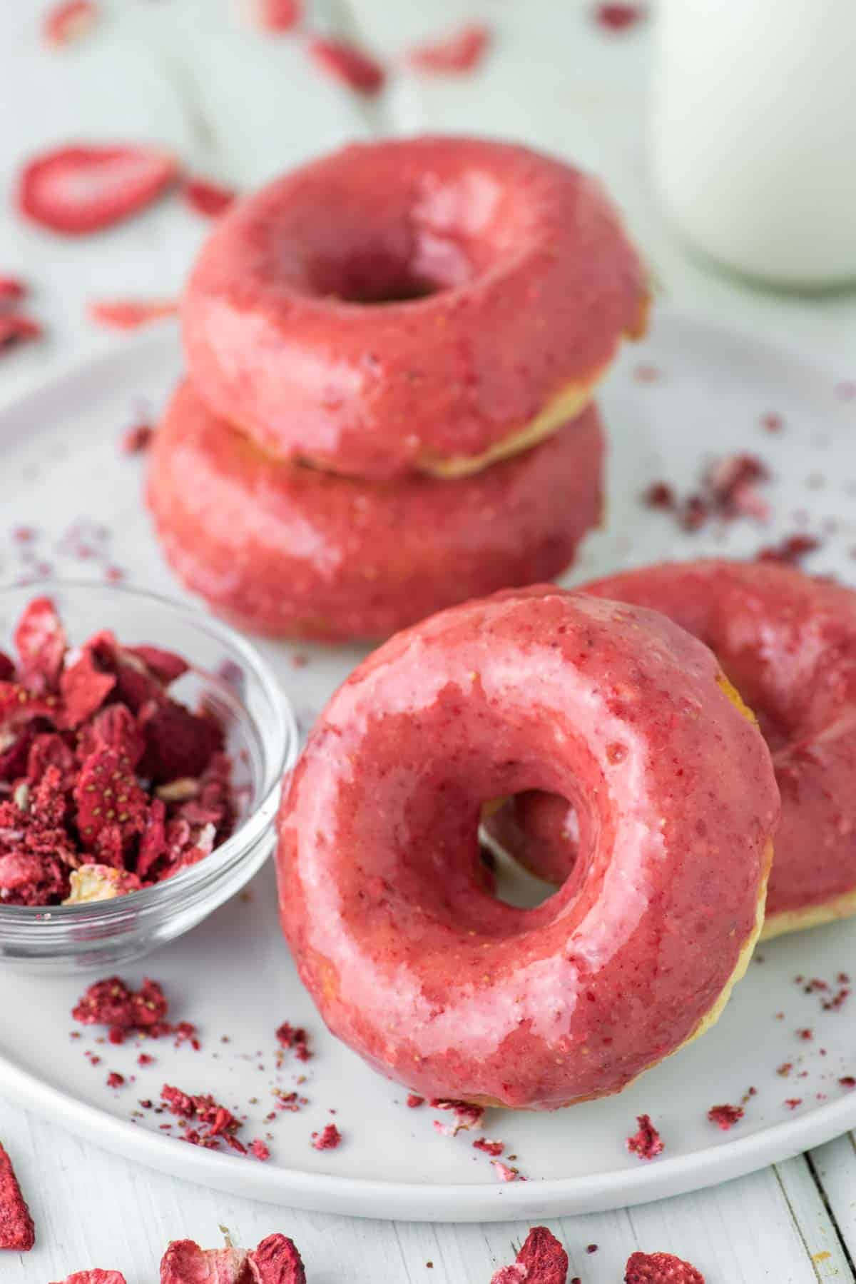 Glazed Donut 桌布 壁紙 — 白色盤子上放著一堆粉紅色糖霜甜甜圈，上面有草莓脆粒，旁邊有一杯牛奶。