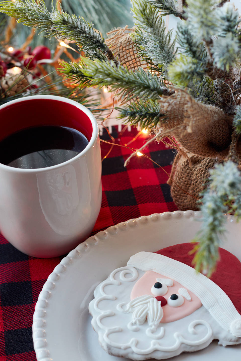 Santa Claus 桌布 壁紙 — 白色盤子上的聖誕老人餅乾、紅色馬克杯、雪松枝和閃爍燈光的節日特寫。