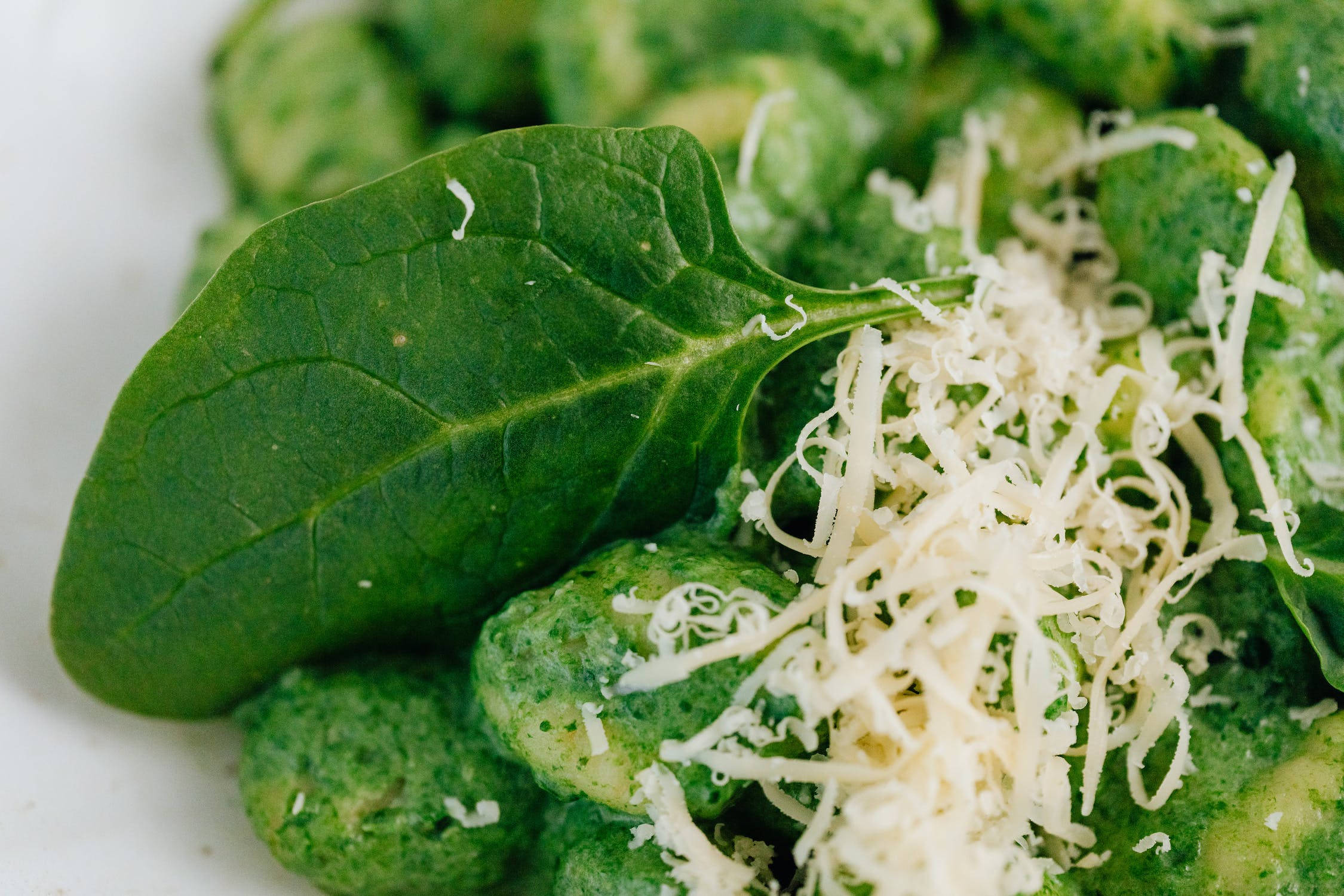 Healthy Food 桌布 壁紙 — 白色盤子上鮮綠色義大利麵疙瘩搭配新鮮菠菜葉和碎起司的特寫。