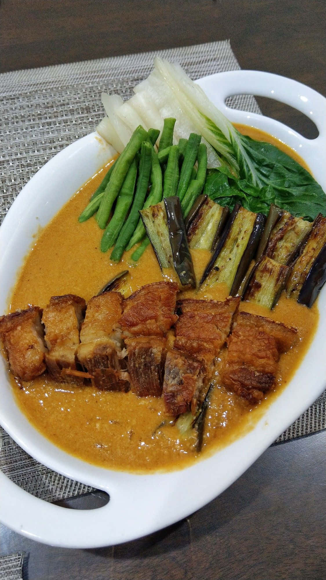 meat 桌布 壁紙 — 白色盤子盛裝著脆皮豬五花肉，搭配濃郁的橙咖哩醬汁、四季豆和茄子，並以菠菜點綴。