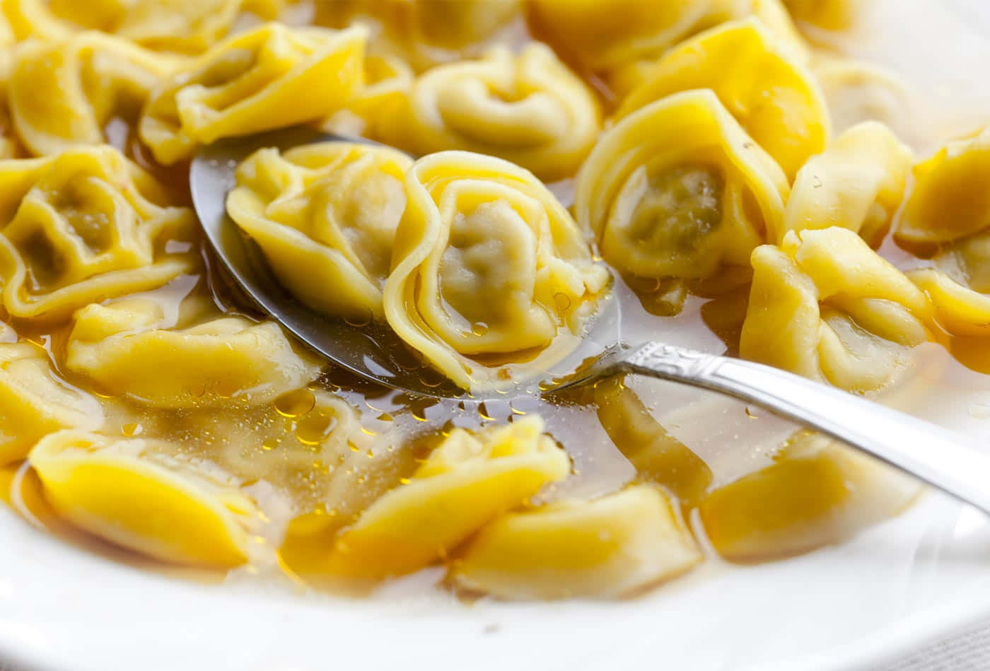 Food Photography 桌布 壁紙 — 白色碗中，濃郁湯汁裡的金色義大利餃子被湯匙舀起的特寫。