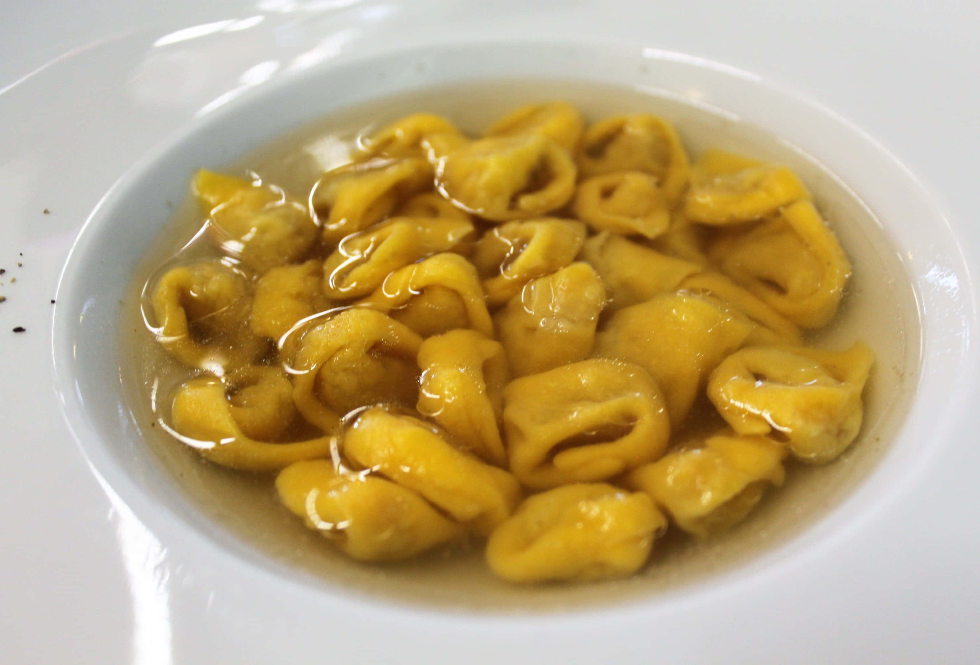 Pasta 桌布 壁紙 — 白色碗中清澈湯汁裡漂浮著金色義大利餃子的特寫，碗邊有少許黑胡椒碎。