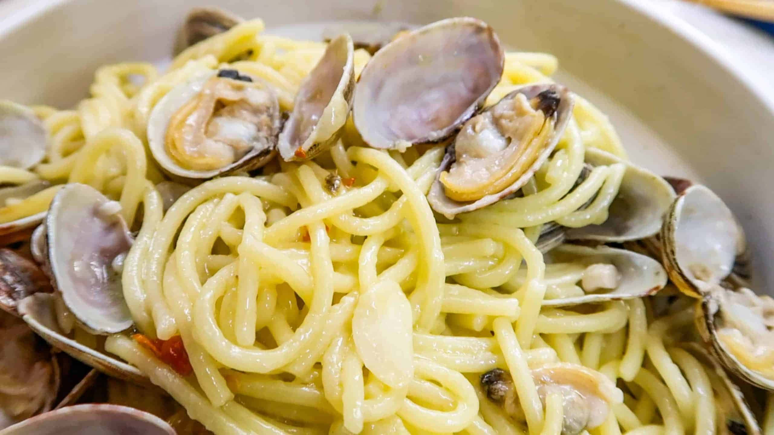 Clam 桌布 壁紙 — 白色碗中的奶油義大利麵和新鮮蛤蜊特寫，醬汁閃亮，並以大蒜裝飾。