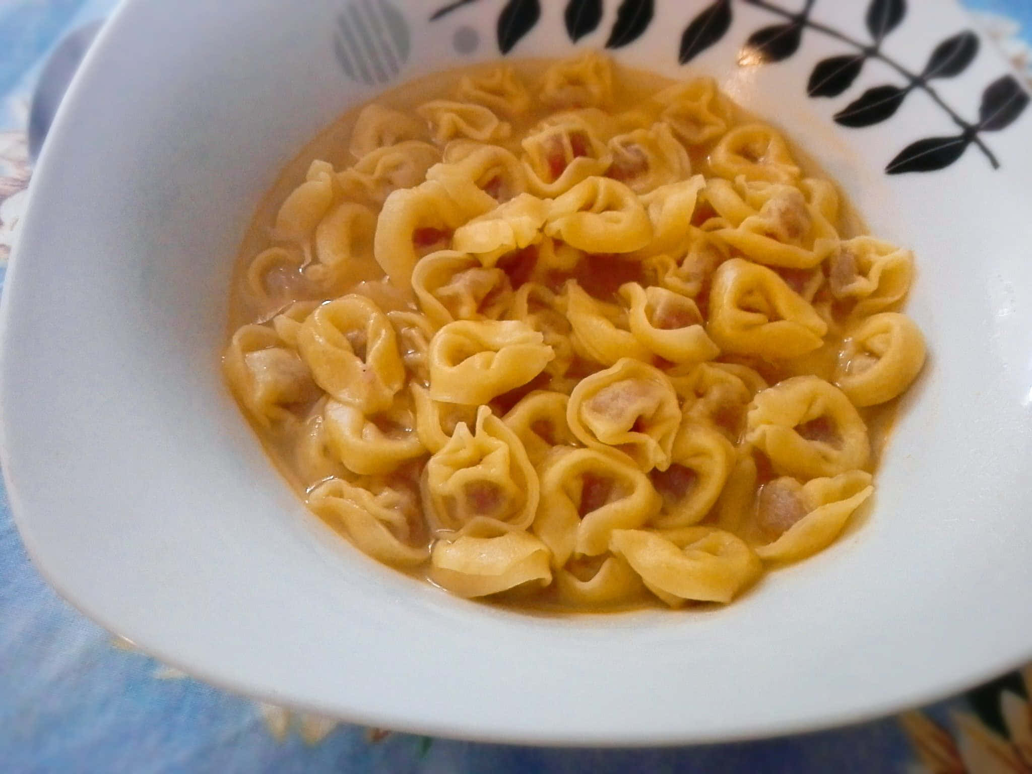 Pasta 桌布 壁紙 — 白色碗中盛載著奶油湯汁的義大利餃（Tortellini）義大利麵特寫，碗邊有黑色葉紋圖案。