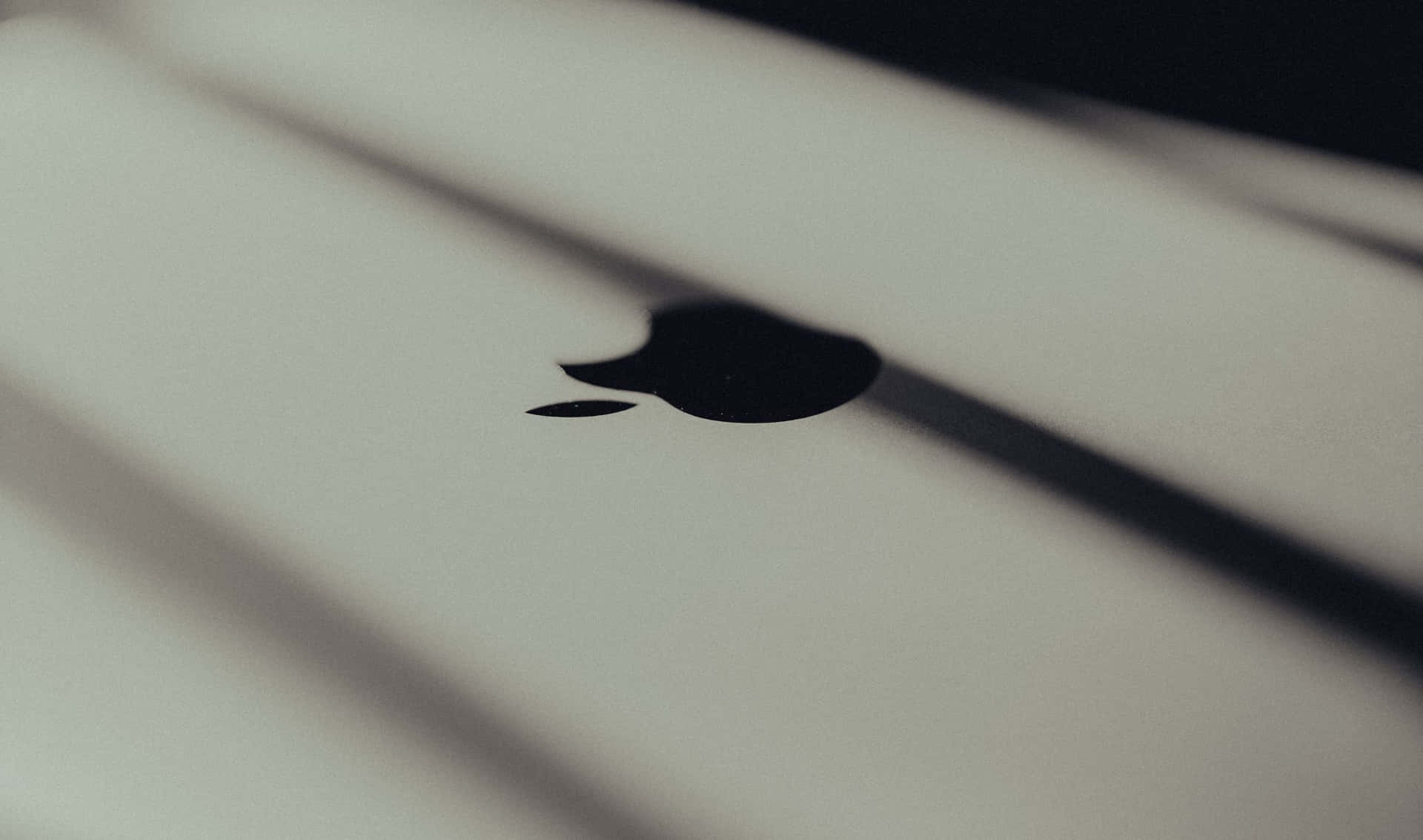 黑白 桌布 壁紙 — 白色筆記型電腦表面上的黑色Apple標誌特寫，帶有柔和的對角陰影。