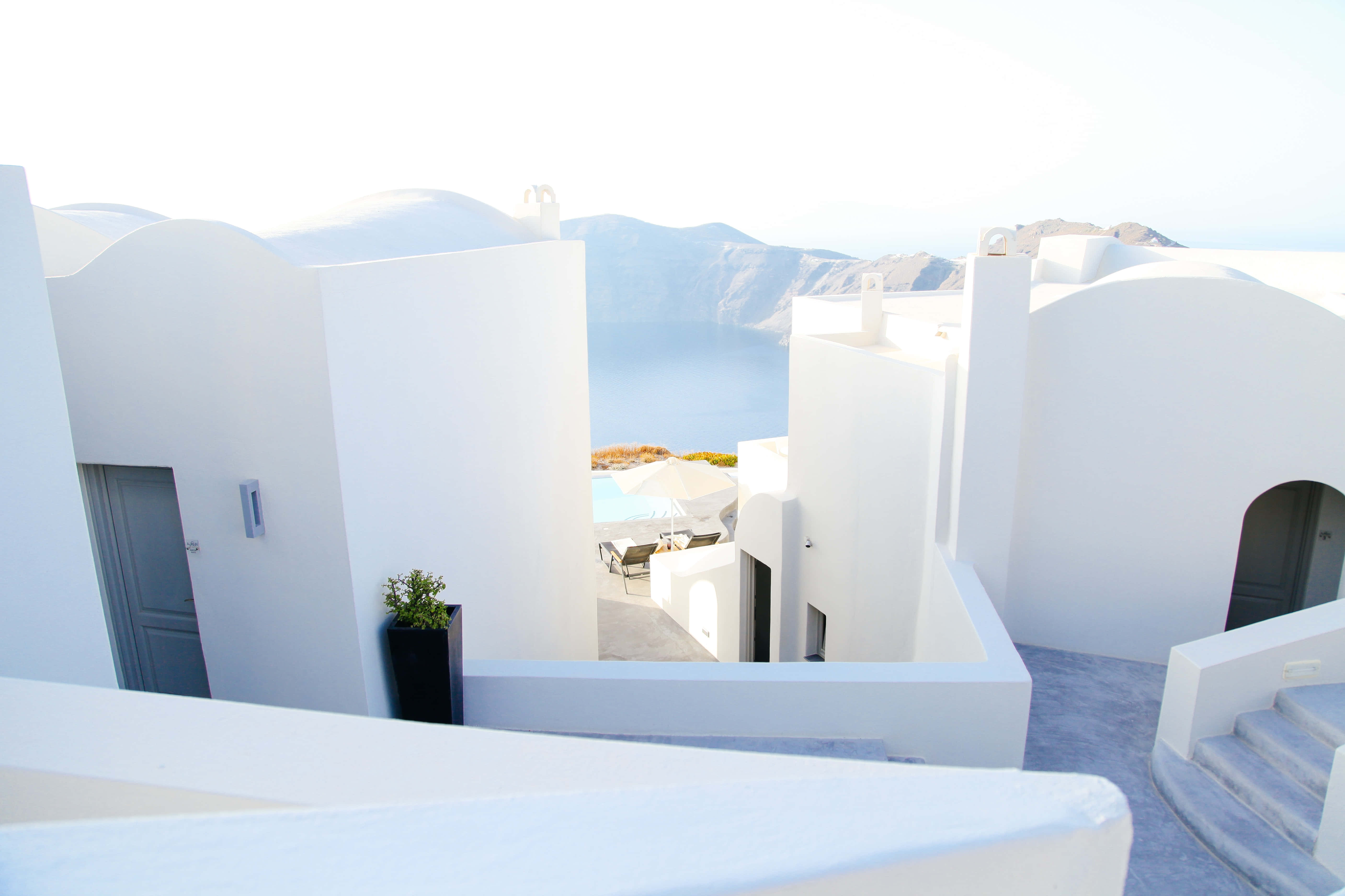 Minimalist Architecture 桌布 壁紙 — 白色粉刷的希臘建築在明亮的日光下框住了愛琴海和遠處火山懸崖的寧靜景色。