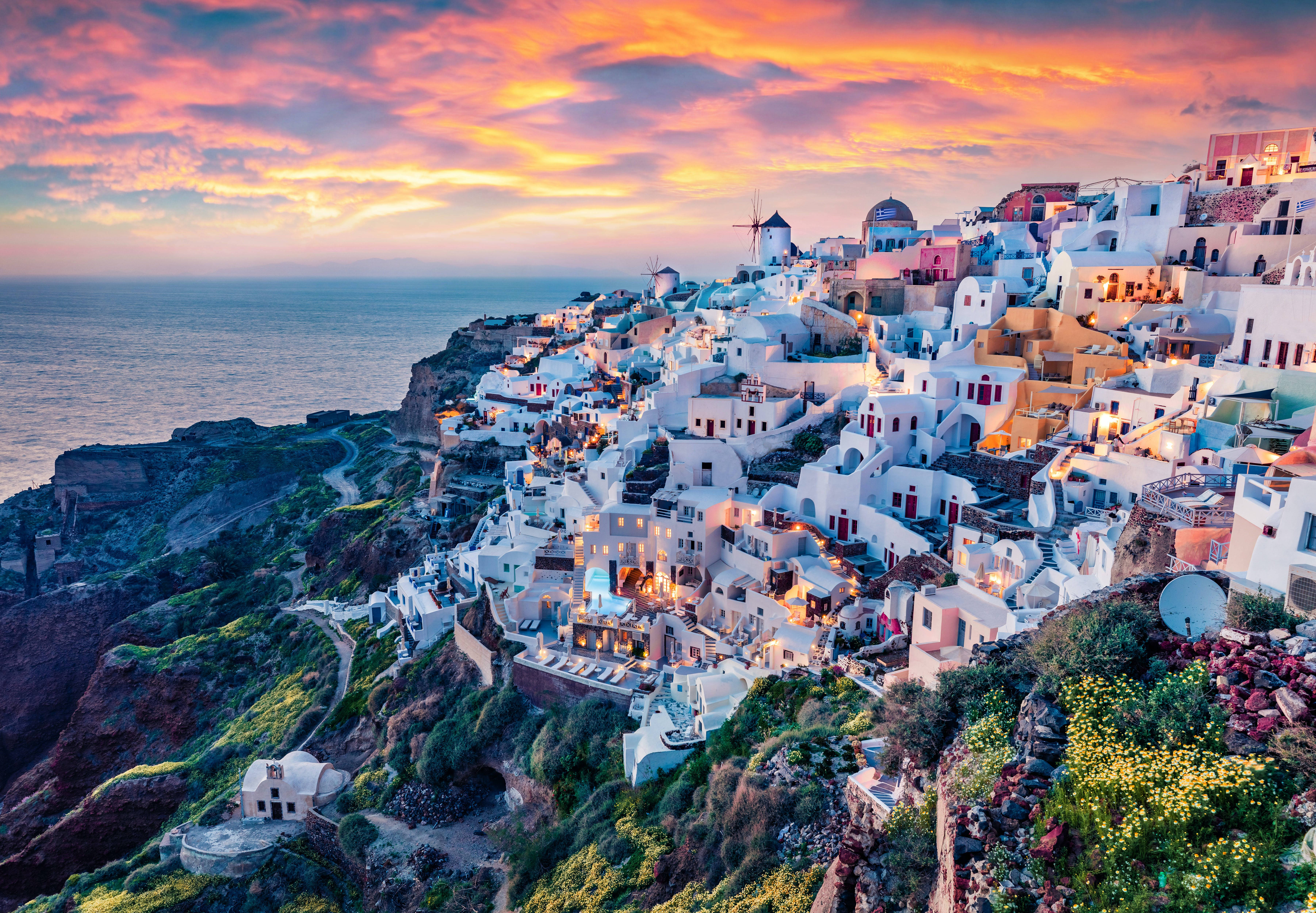 Santorini 桌布 壁紙 — 白色粉刷的懸崖村莊在日落時閃耀，天空火紅橙黃，下方平靜的海面。