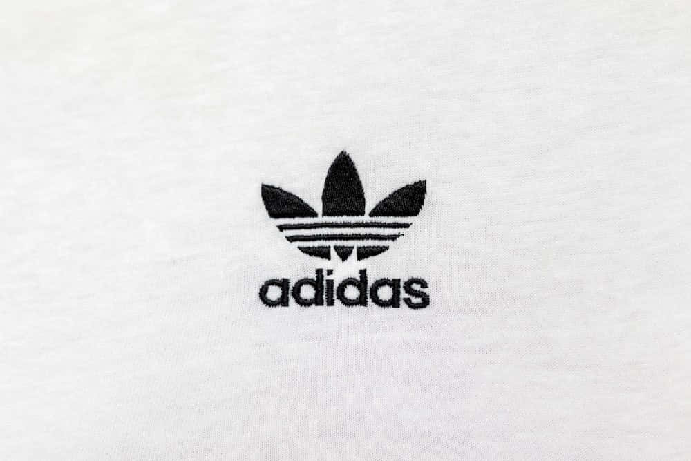 愛迪達 桌布 壁紙 — 白色紋理布料背景上黑色刺繡Adidas標誌的特寫。