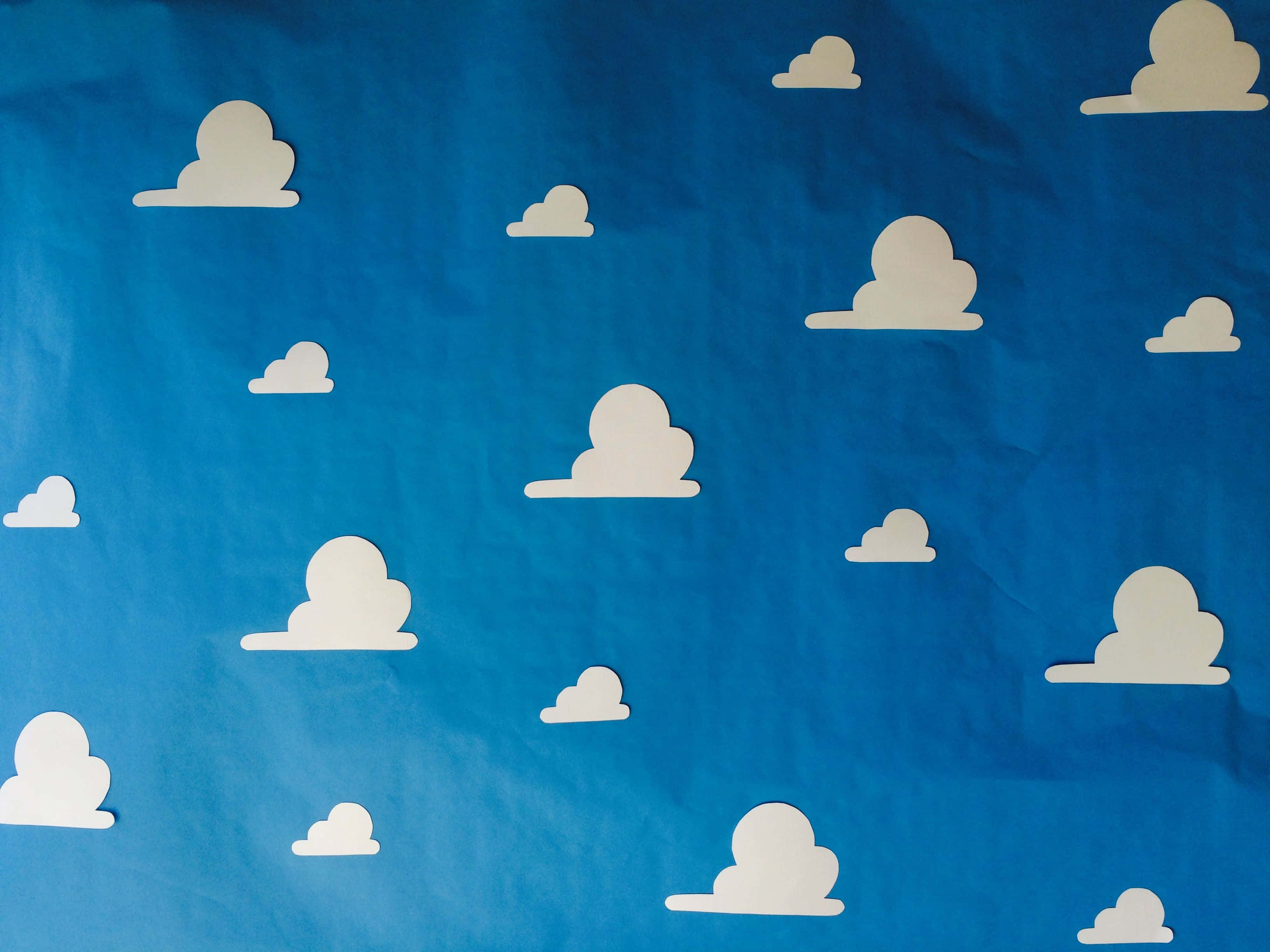 Toy Story Cloud 桌布 壁紙 — 白色紙雲漂浮在帶有紋理的藍色紙天空上，形成俏皮的極簡圖案。