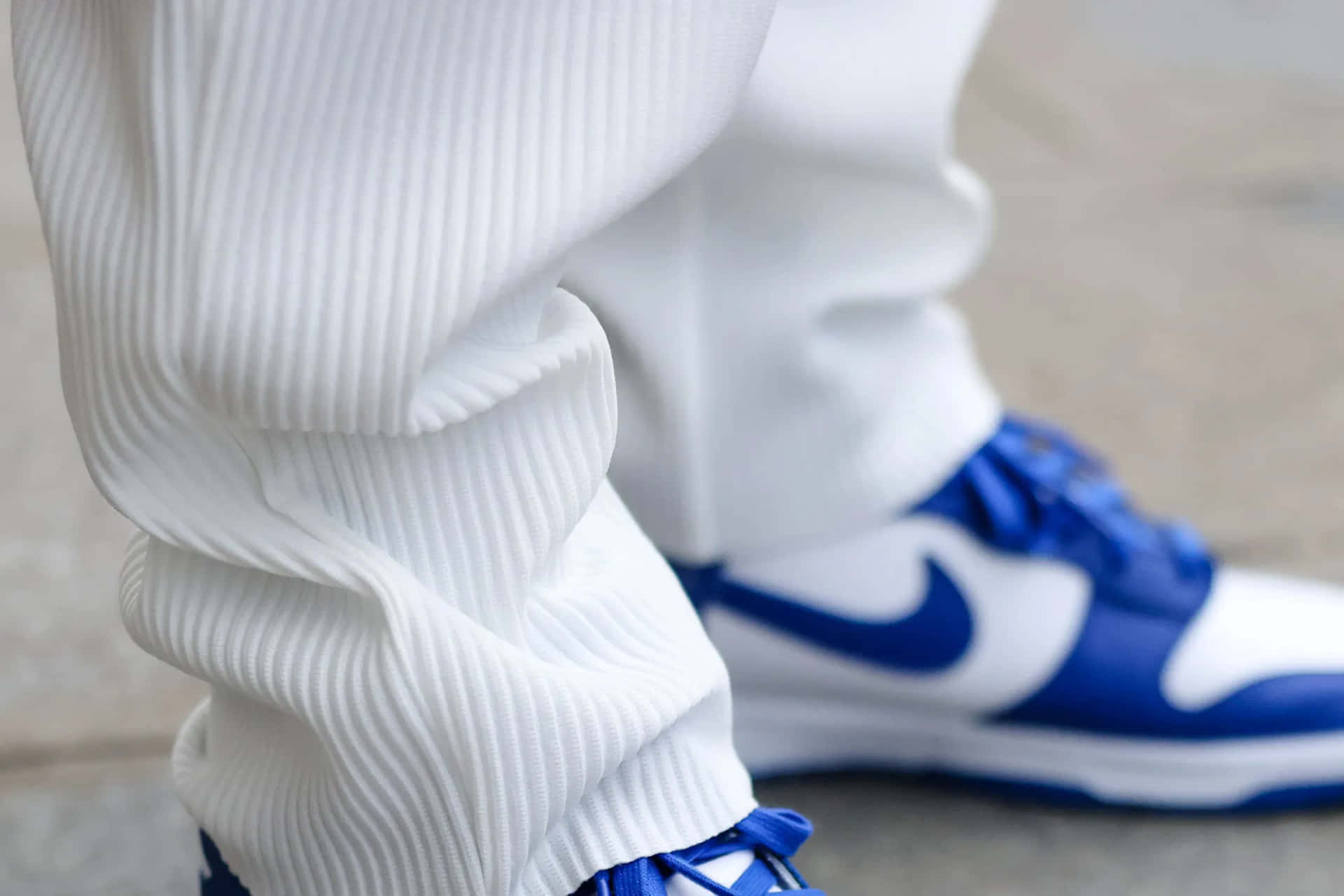 Nike 桌布 壁紙 — 白色羅紋慢跑褲和皇家藍色和白色Nike運動鞋在混凝土表面上的特寫。