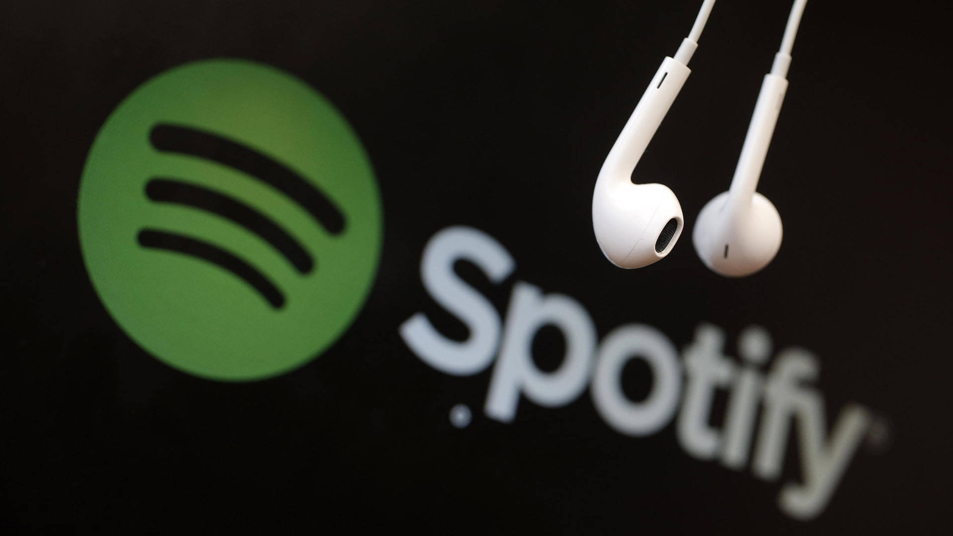 Spotify 桌布 壁紙 — 白色耳機懸掛在黑暗螢幕上發光的Spotify標誌上方。