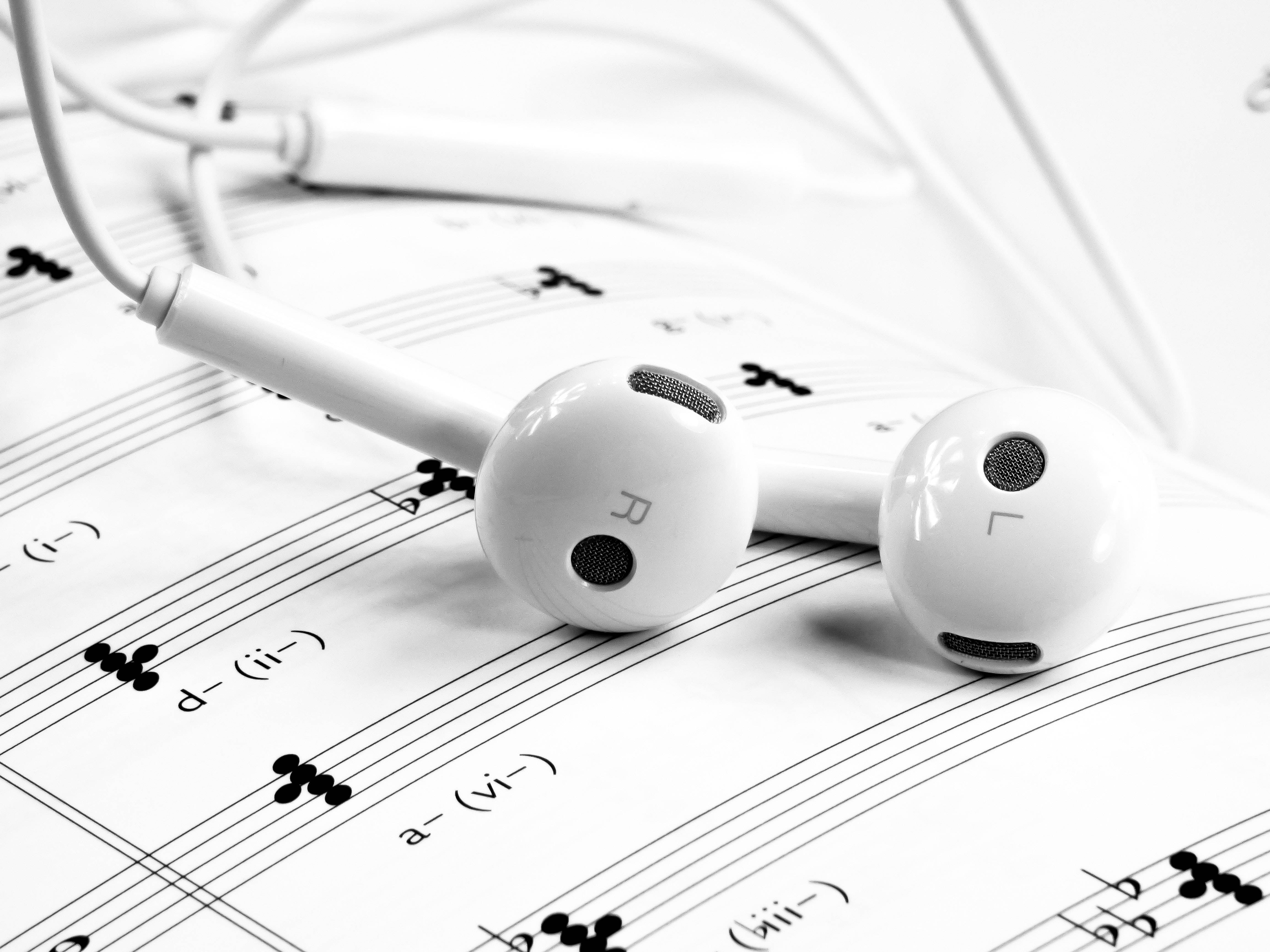 音樂 桌布 壁紙 — 白色耳機放在樂譜上，單色特寫強調音樂細節和乾淨線條。