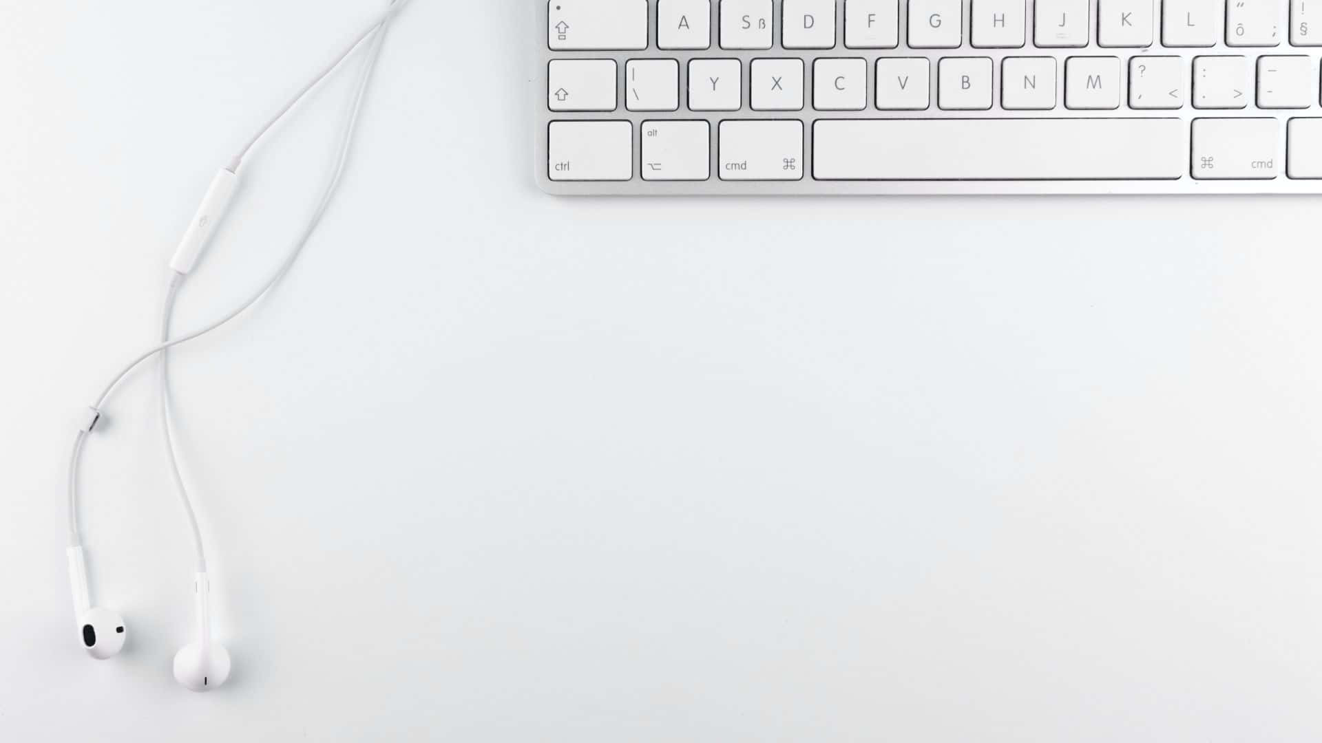 White Aesthetic Laptop 桌布 壁紙 — 白色耳機放在簡約白色桌面上，旁邊是一個時尚的銀色鍵盤。