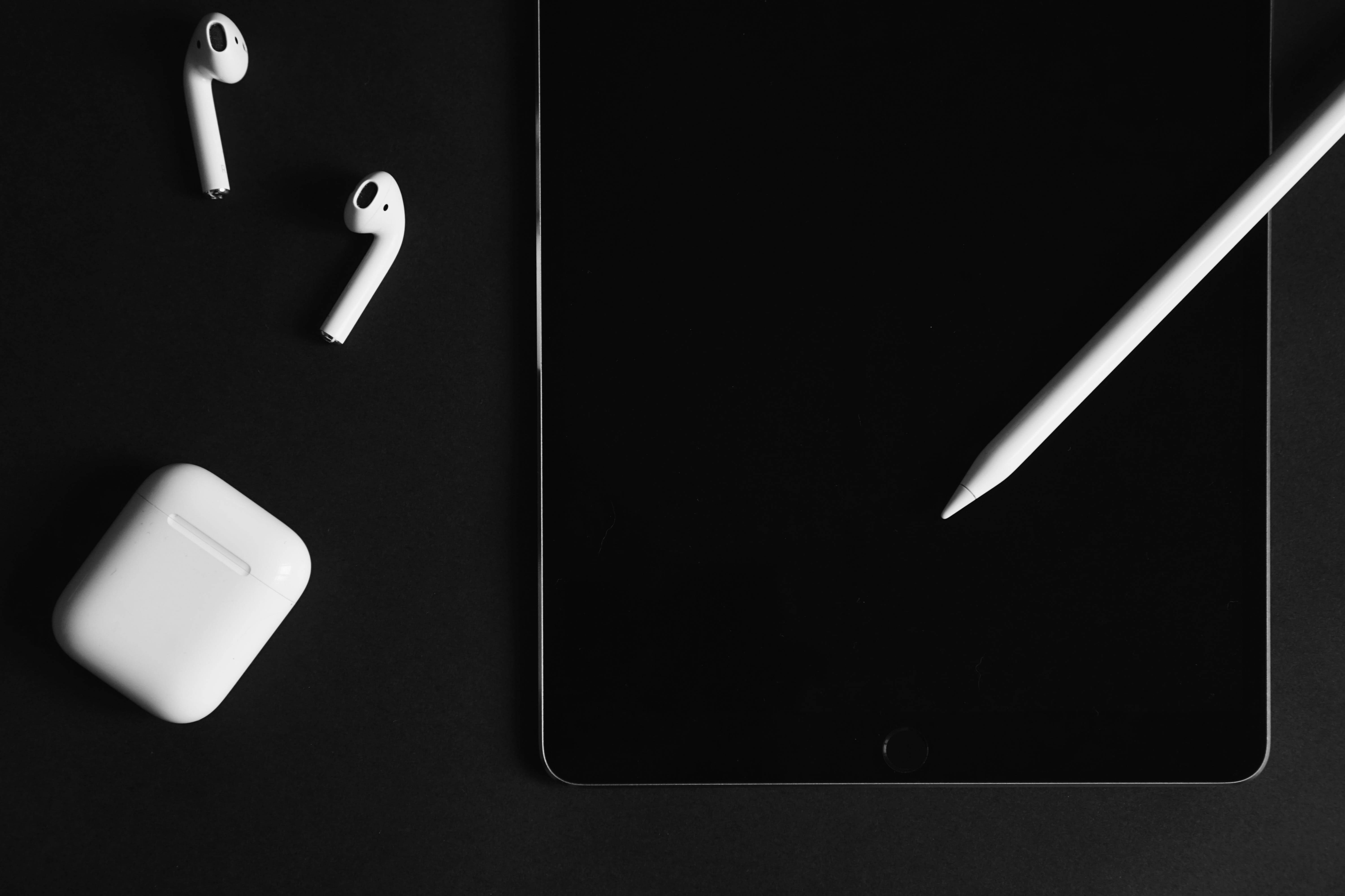 AirPods 桌布 壁紙 — 白色耳機盒和觸控筆放在時尚的黑色平板電腦上，背景是極簡的深色表面。