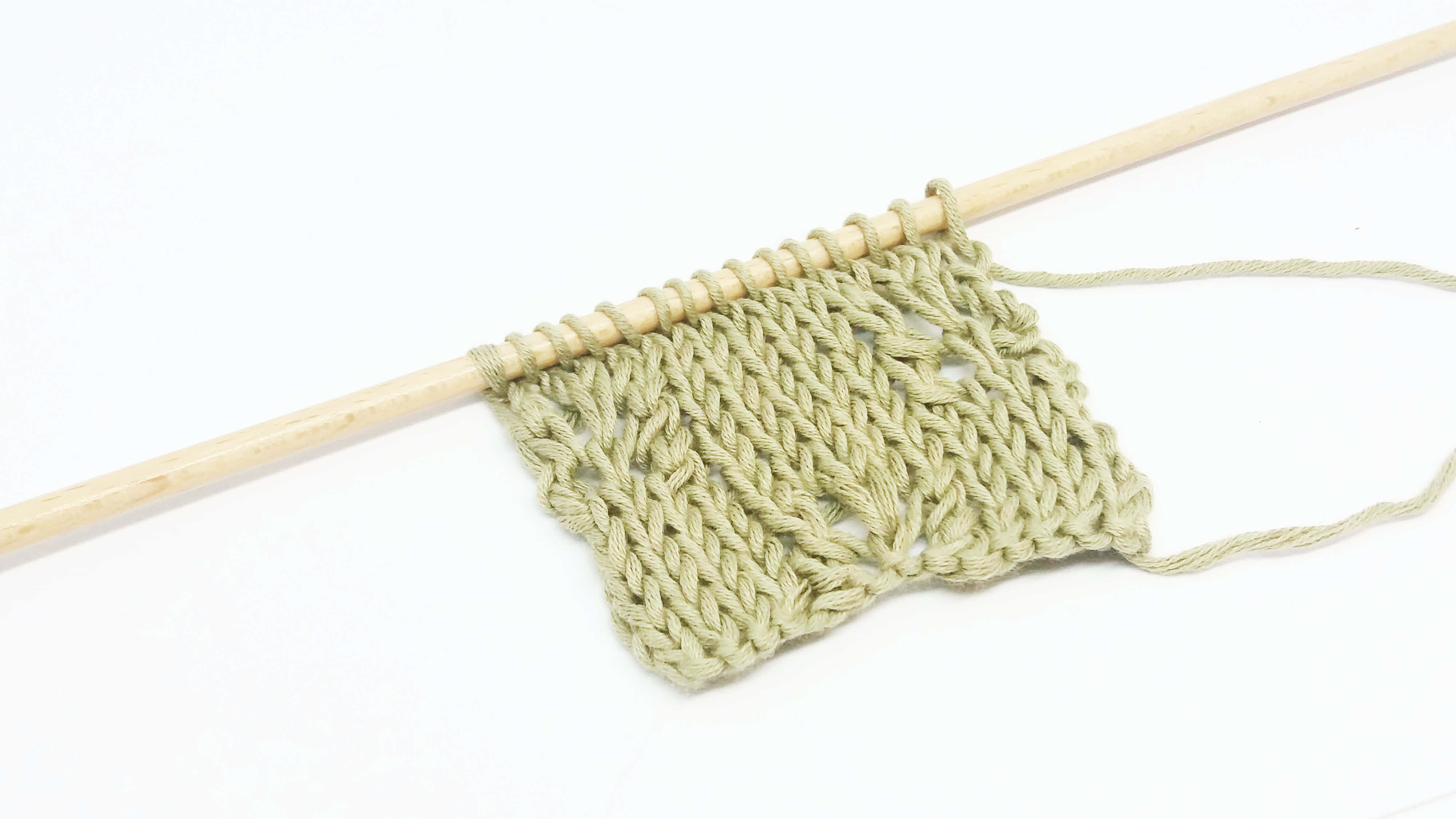 Butterfly Stitch 桌布 壁紙 — 白色背景上，木製織針上淺綠色針織布料帶有蕾絲圖案的近距離特寫。