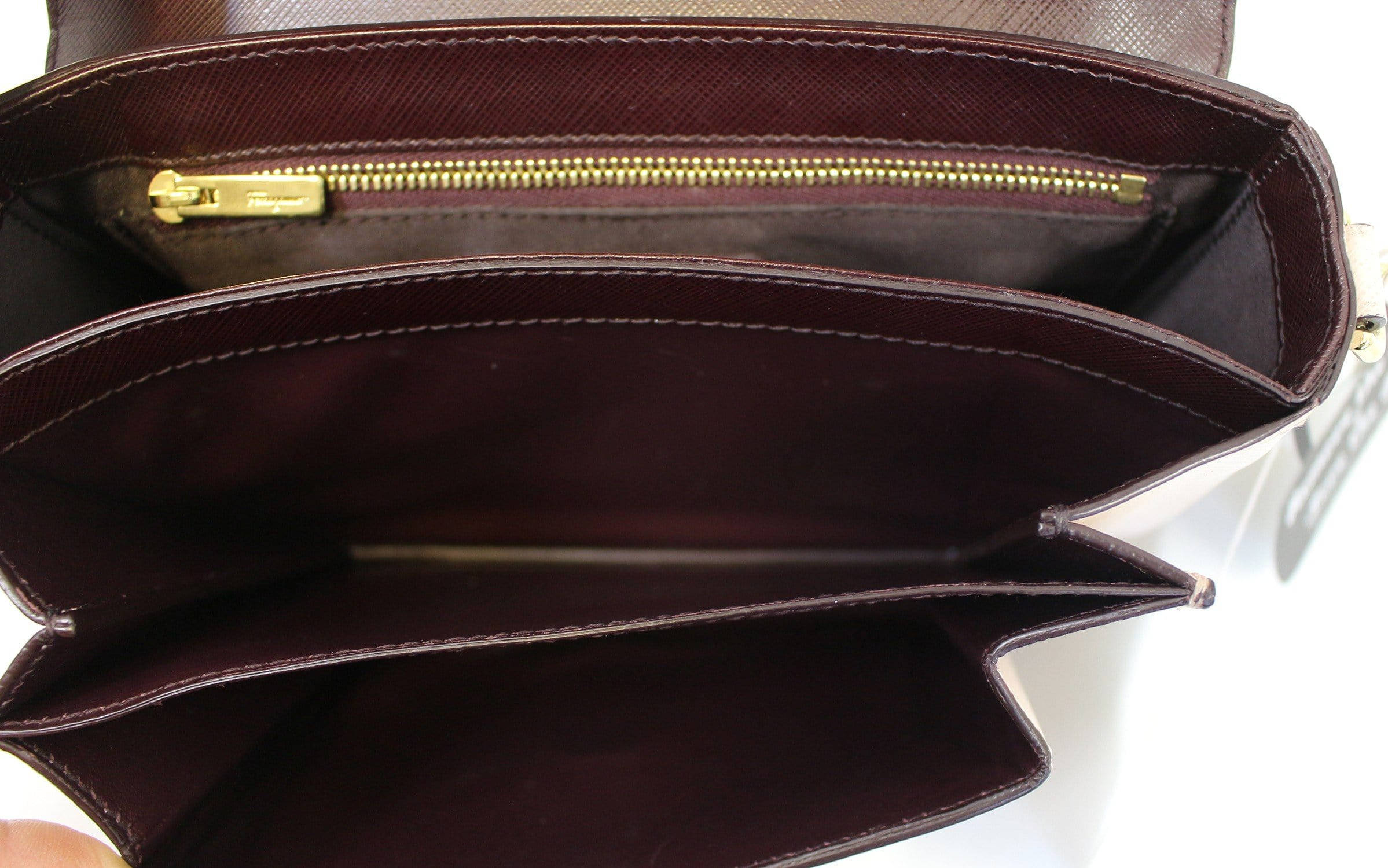 Ferragamo 桌布 壁紙 — 白色背景上，酒紅色皮革錢包配金色拉鍊和整齊縫線的特寫。