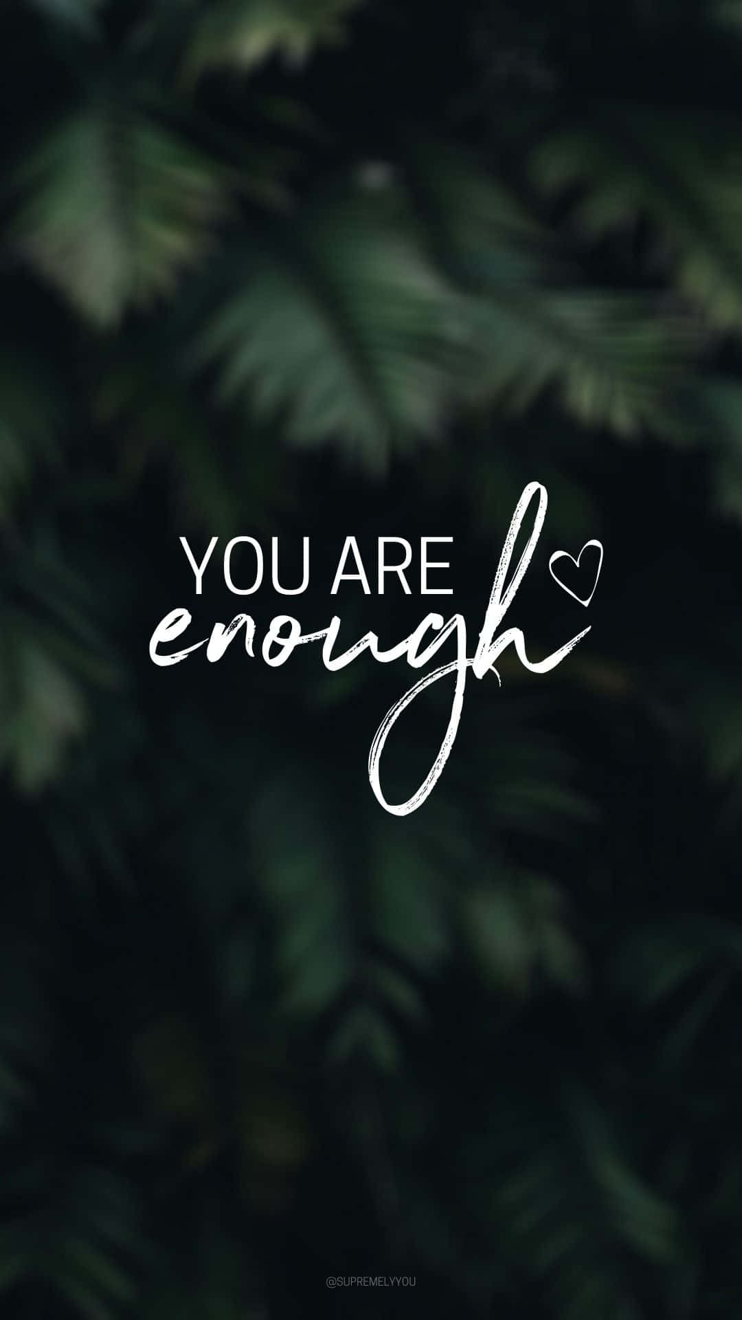 Quote 桌布 壁紙 — 白色草書文字 'you are enough' 帶有心形裝飾，漂浮在模糊的深綠色樹葉背景上。
