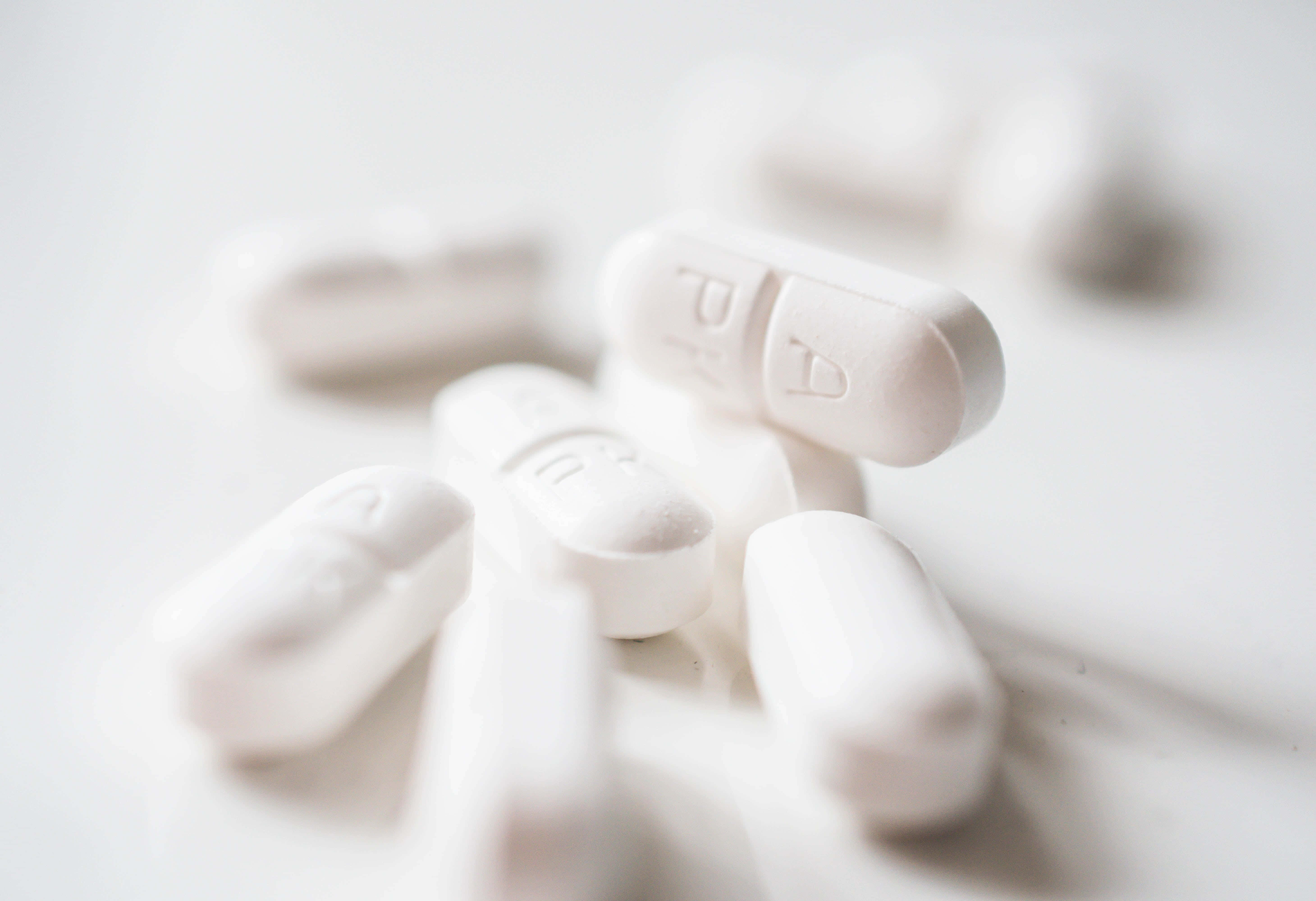 pills 桌布 壁紙 — 白色藥丸特寫，帶有壓花字母，散落在明亮的白色表面上，景深較淺。