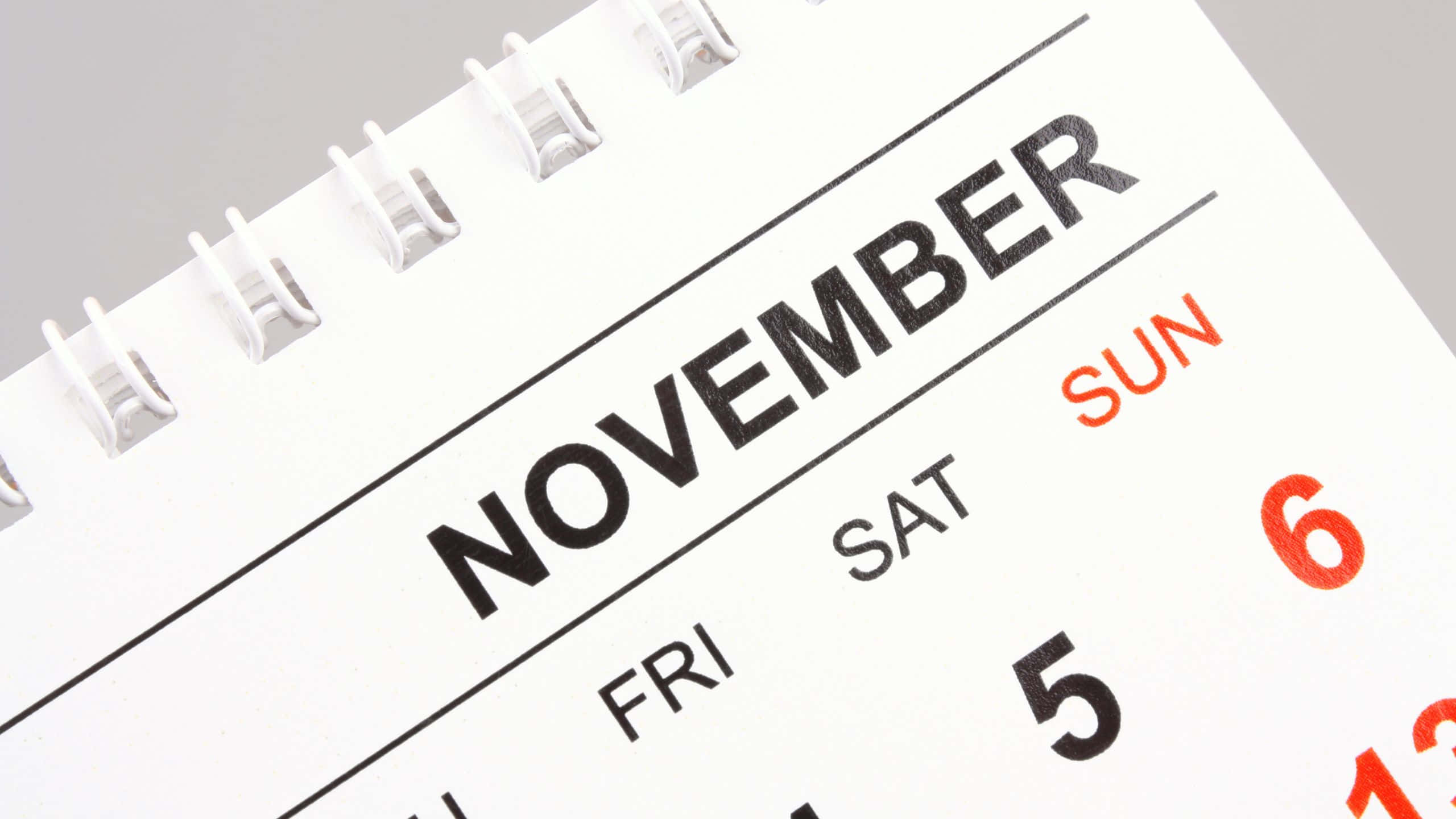 November Desktop 桌布 壁紙 — 白色螺旋裝訂日曆的特寫，顯示十一月，在乾淨的紙張上有粗體黑色和紅色文字。