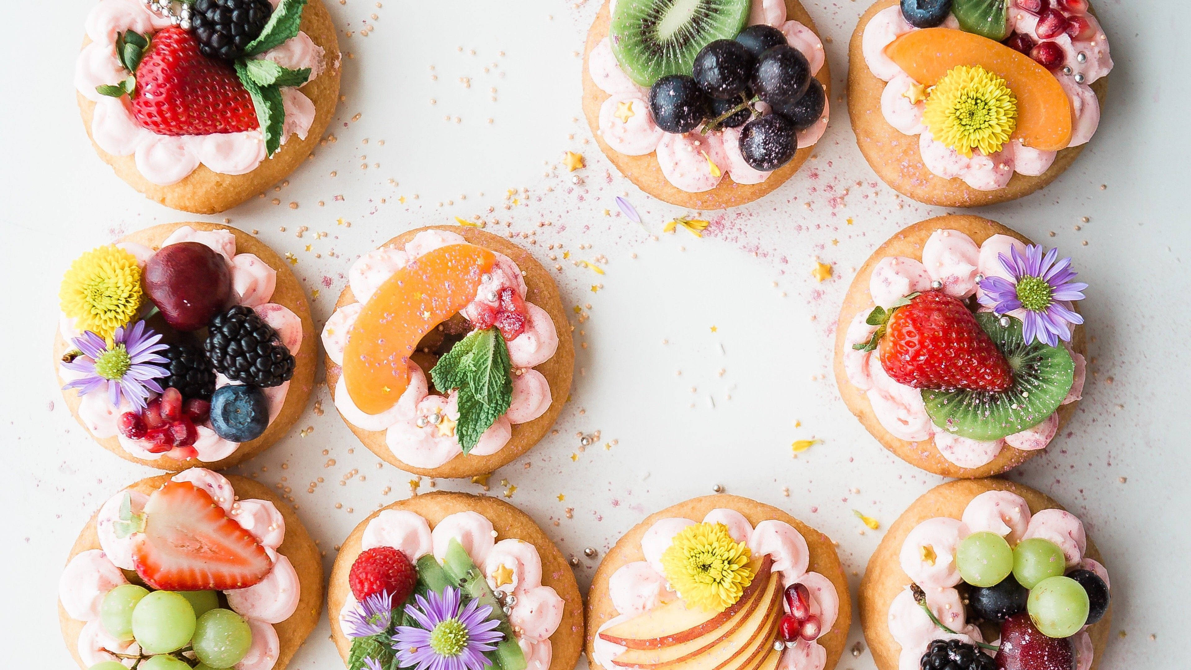 Pastry 桌布 壁紙 — 白色表面上九個色彩繽紛的迷你塔，上面鋪滿新鮮水果和食用花的俯拍照片。